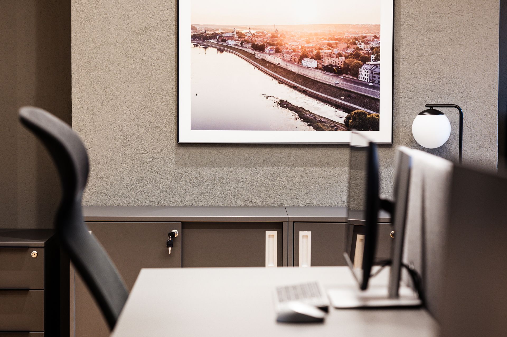 Stalas su kompiuteriu ir paveikslu ant sienos virš jo