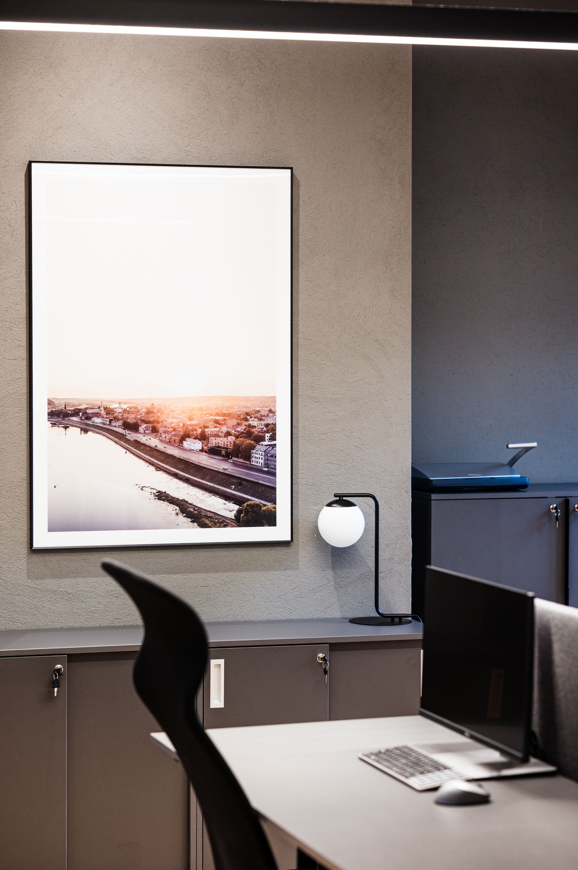 Stalas su kompiuteriu ir paveikslu ant sienos virš jo.