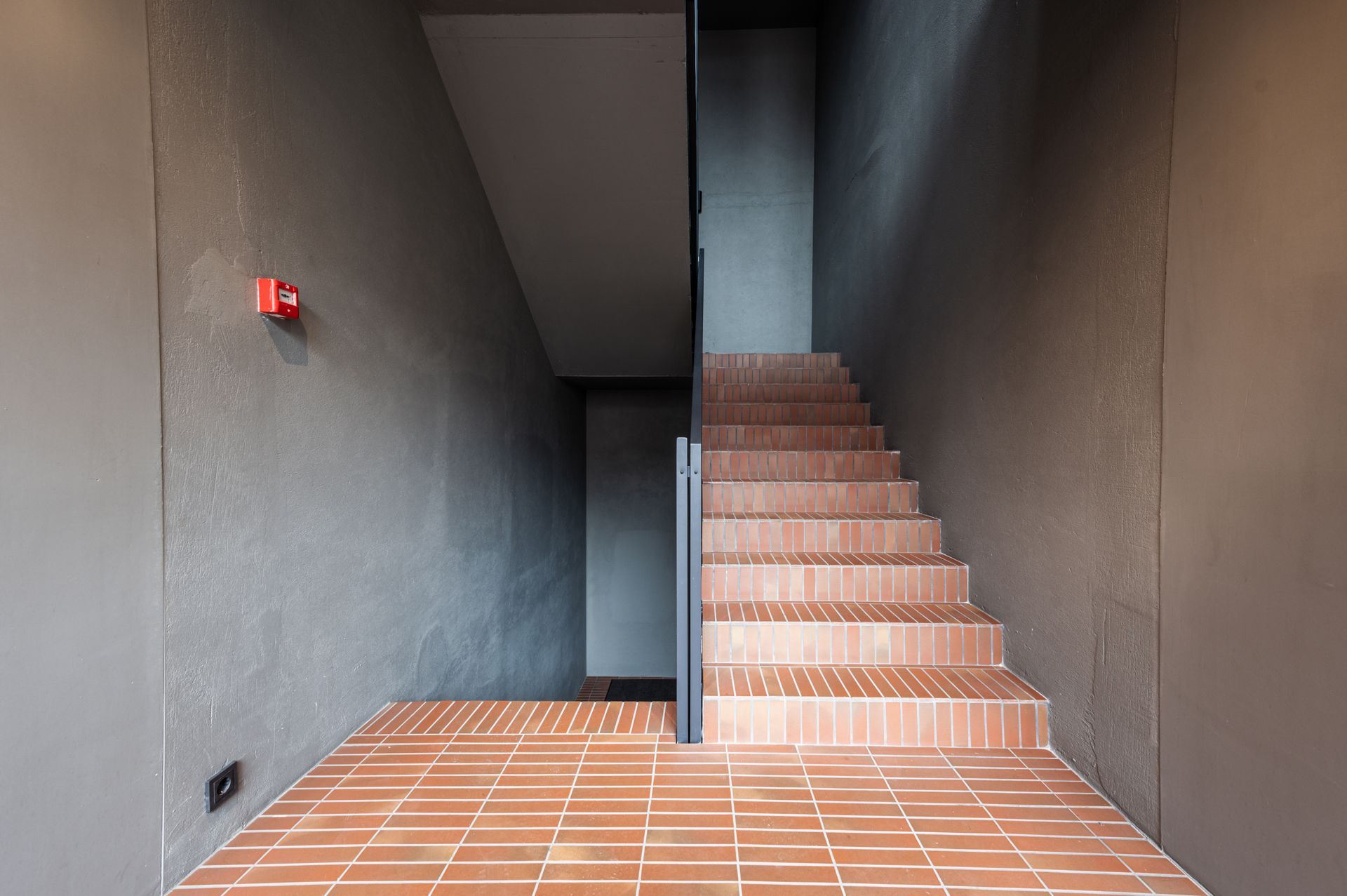 Laiptai su plytų pakopomis ir priešgaisrine signalizacija ant sienos.