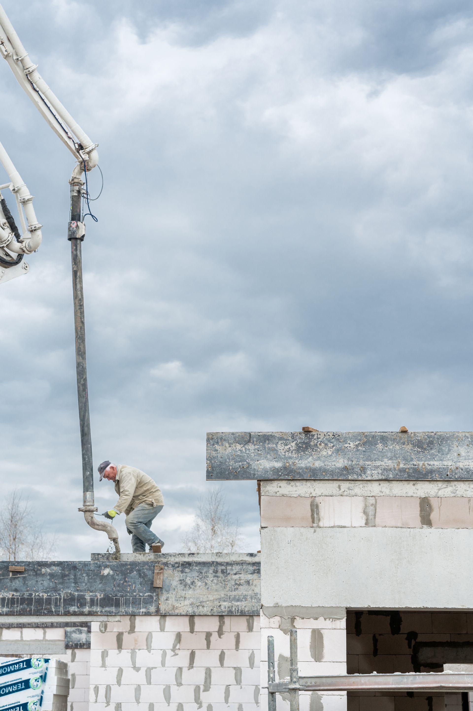 Vyras stovi ant pastato stogo, o kranas į jį pumpuoja cementą.