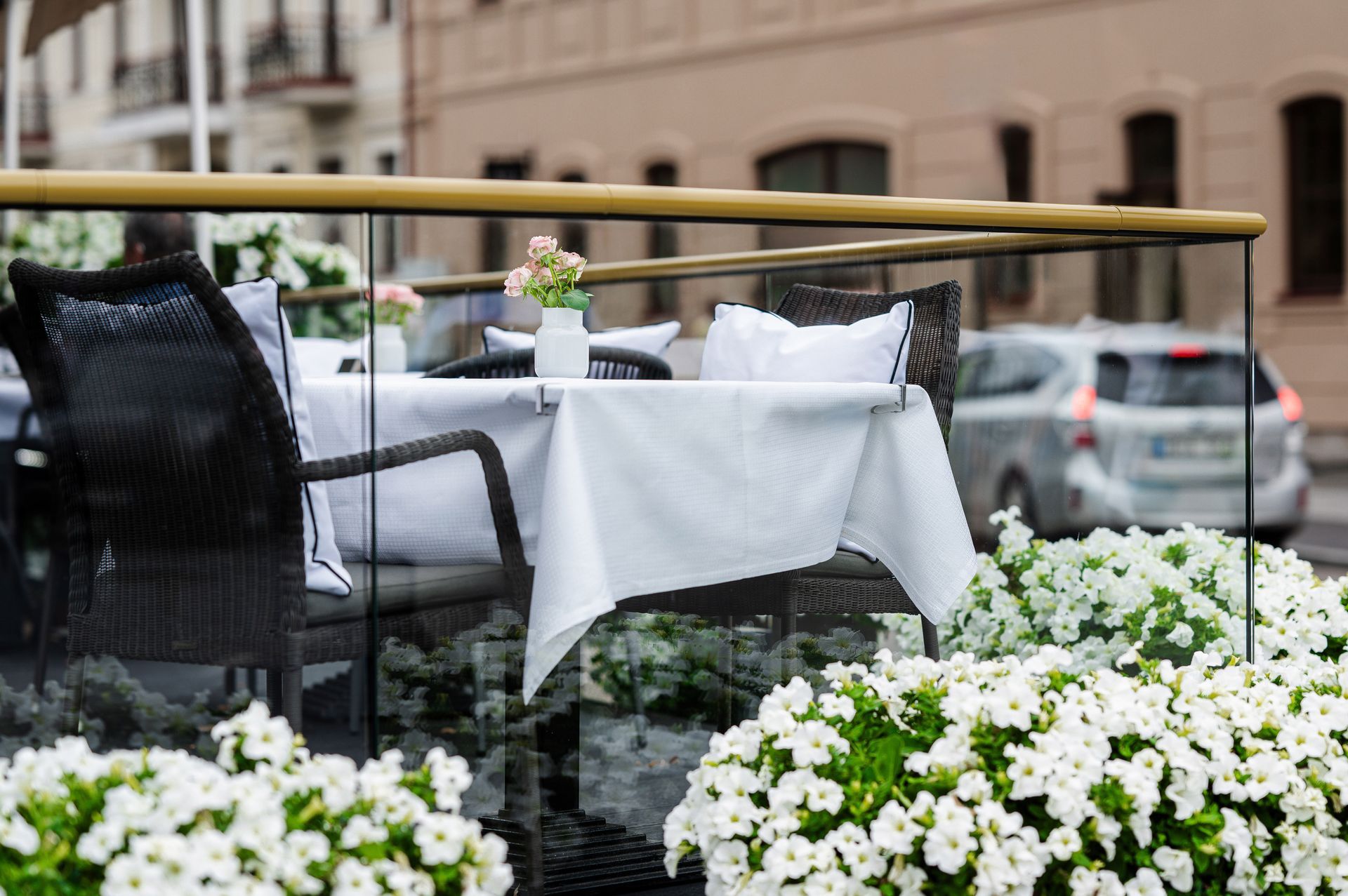 Stalas su balta staltiese ir kėdėmis balkone, apsuptame baltų gėlių.