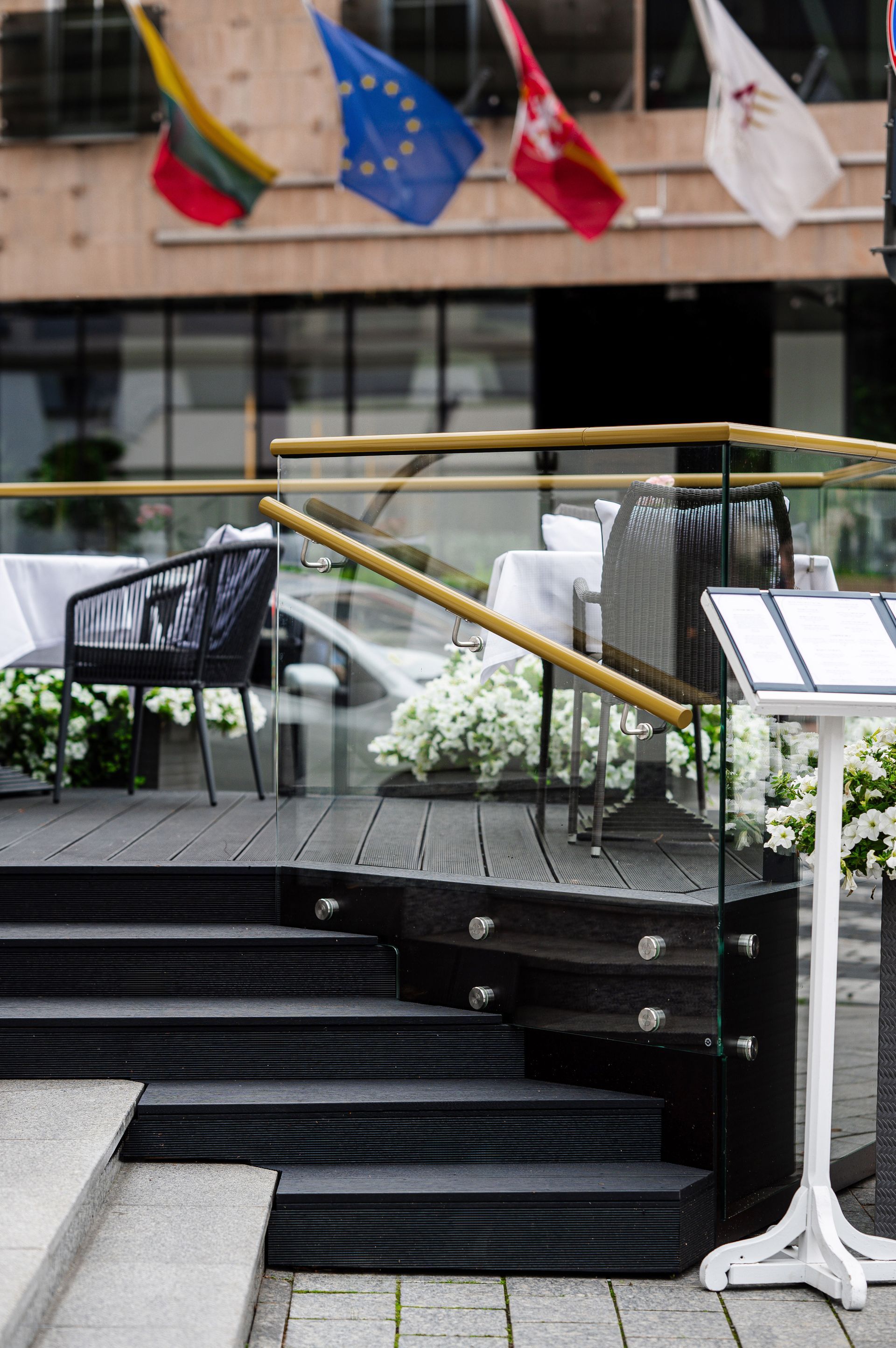 Restoranas su laiptais, vedančiais į balkoną, kurio fone plevėsuoja vėliavos.