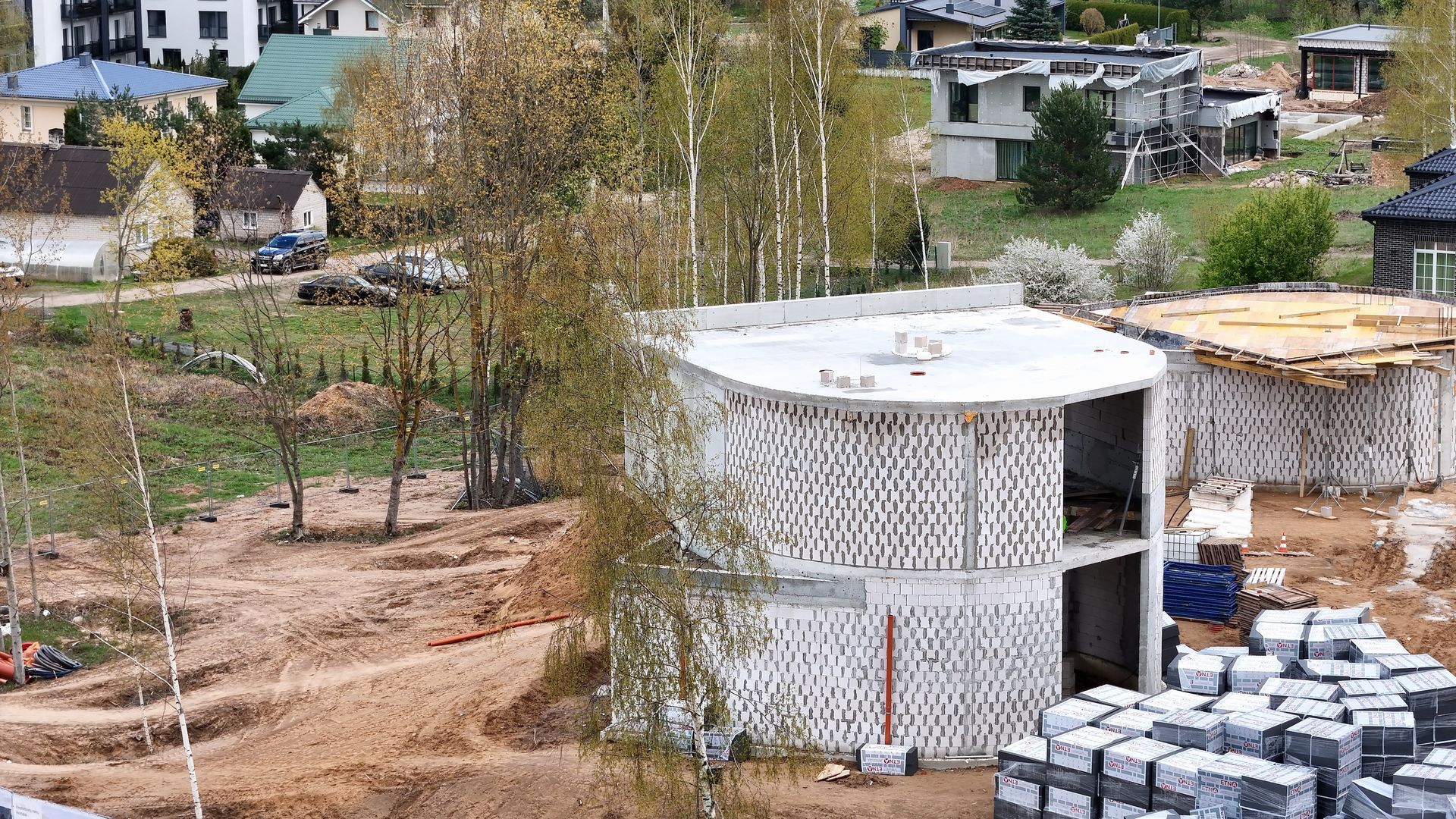 Didelis baltas pastatas statomas purvo lauko viduryje.