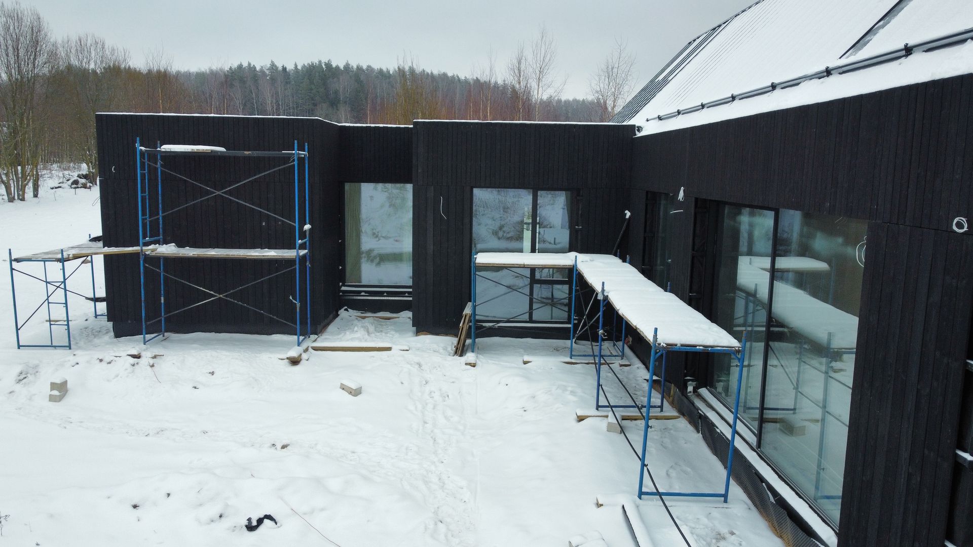 Sniege statomas juodas namas su aplink jį esančiais pastoliais.
