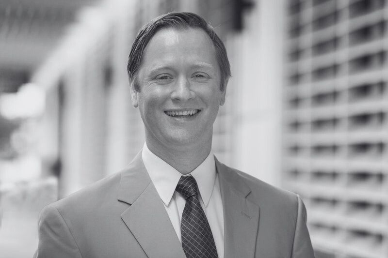 Smiling man in a suit and tie standing outdoors near a building