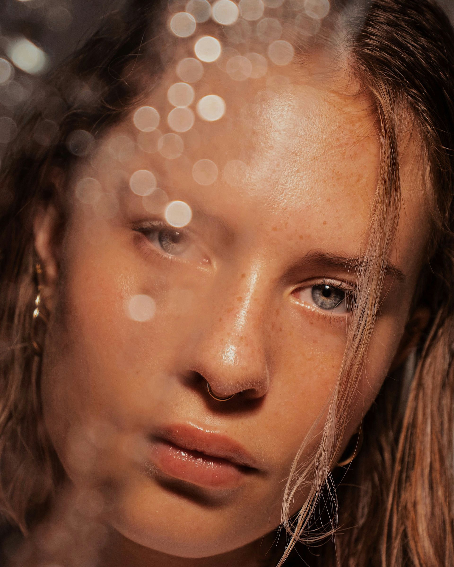 Close-up portrait of a person behind sparkling water droplets, with a soft, reflective expression