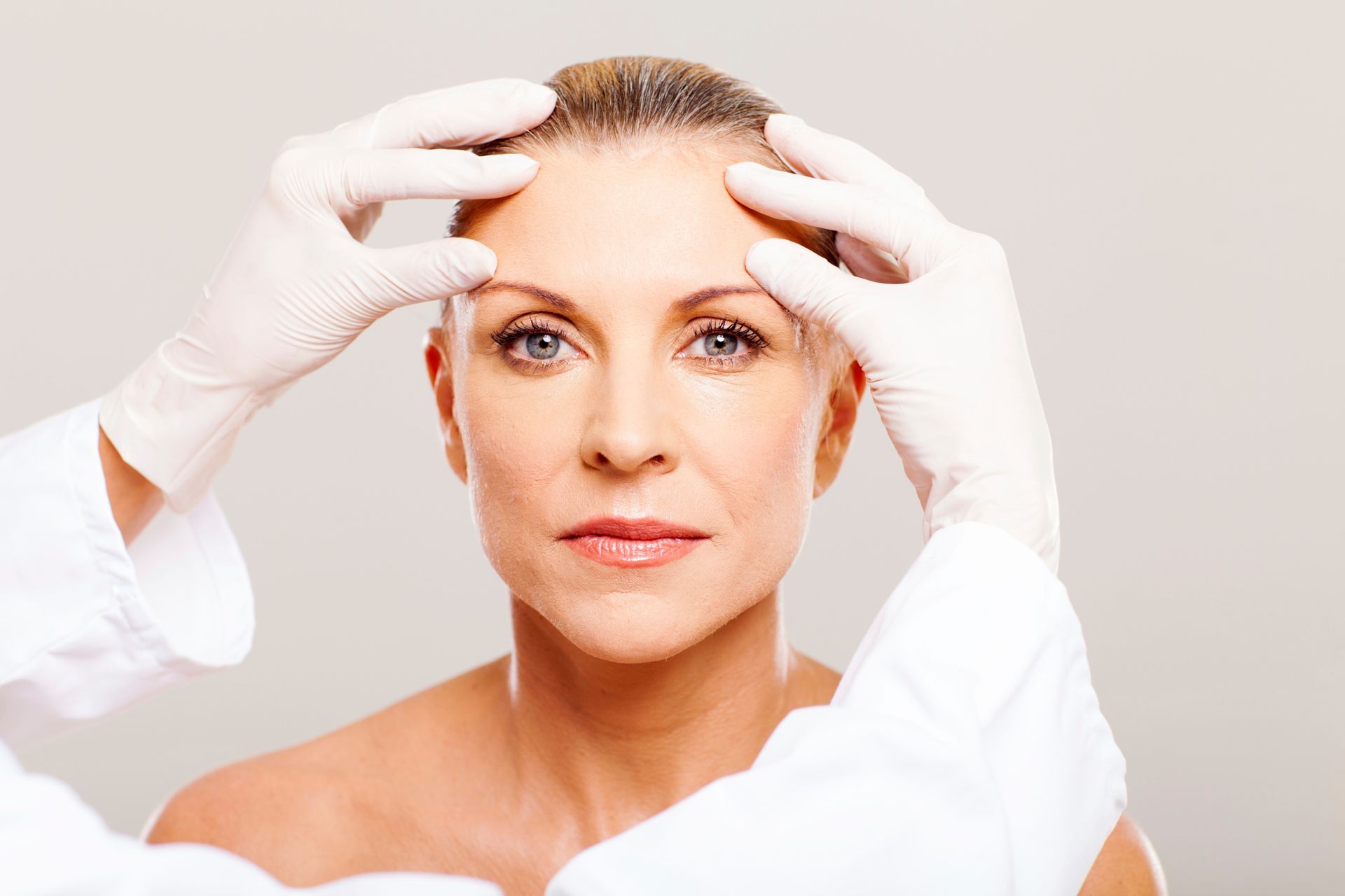 Gloved hands examining a person’s forehead during a cosmetic procedure
