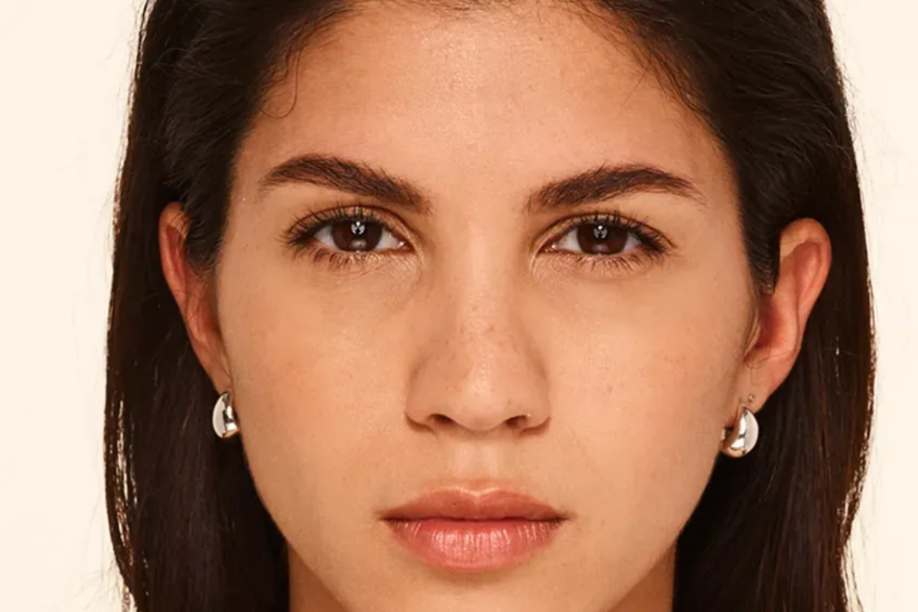 Close-up portrait of a woman with dark hair, neutral expression, and small earrings