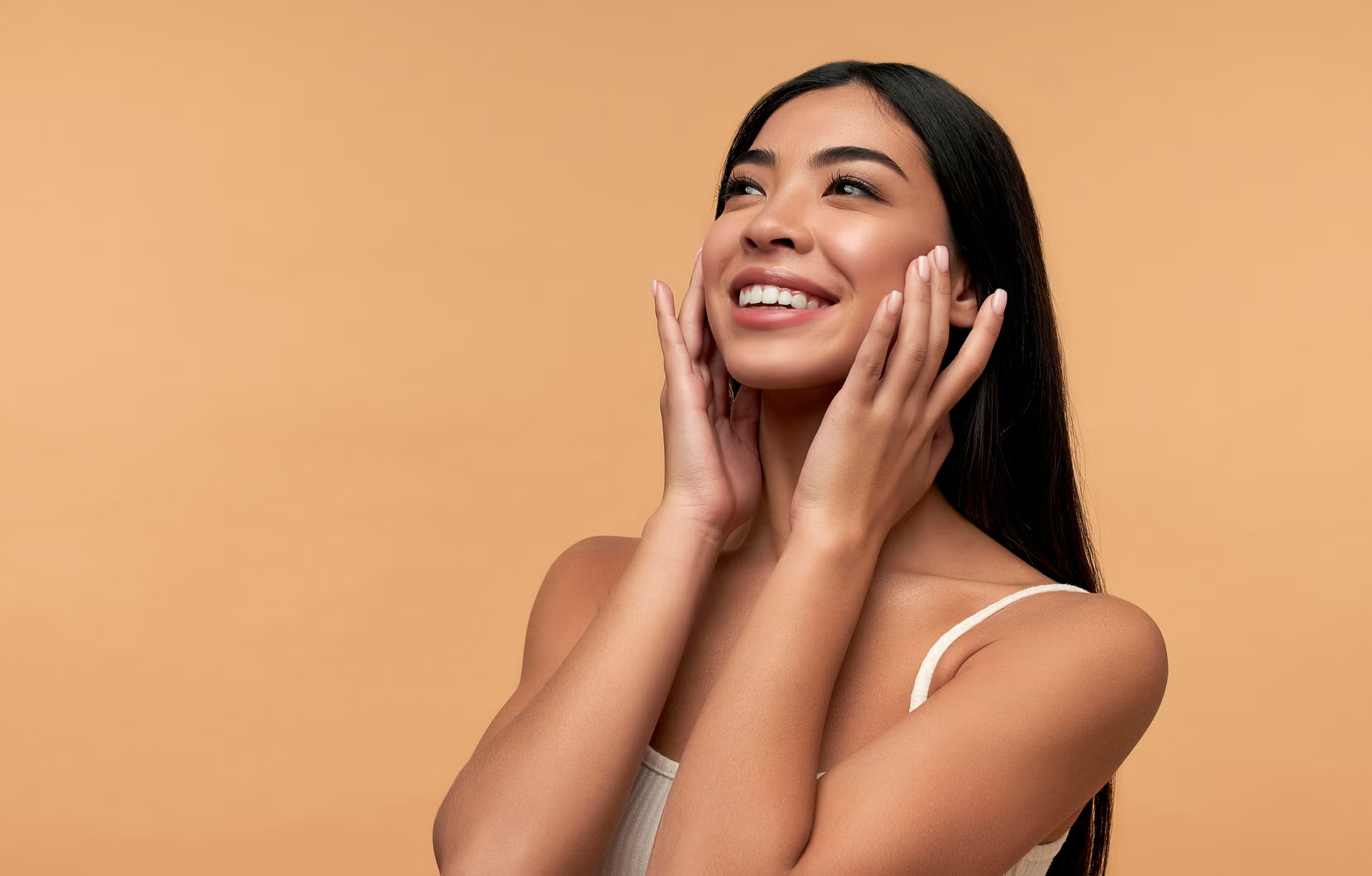 Smiling woman with hands on her face against a warm orange background