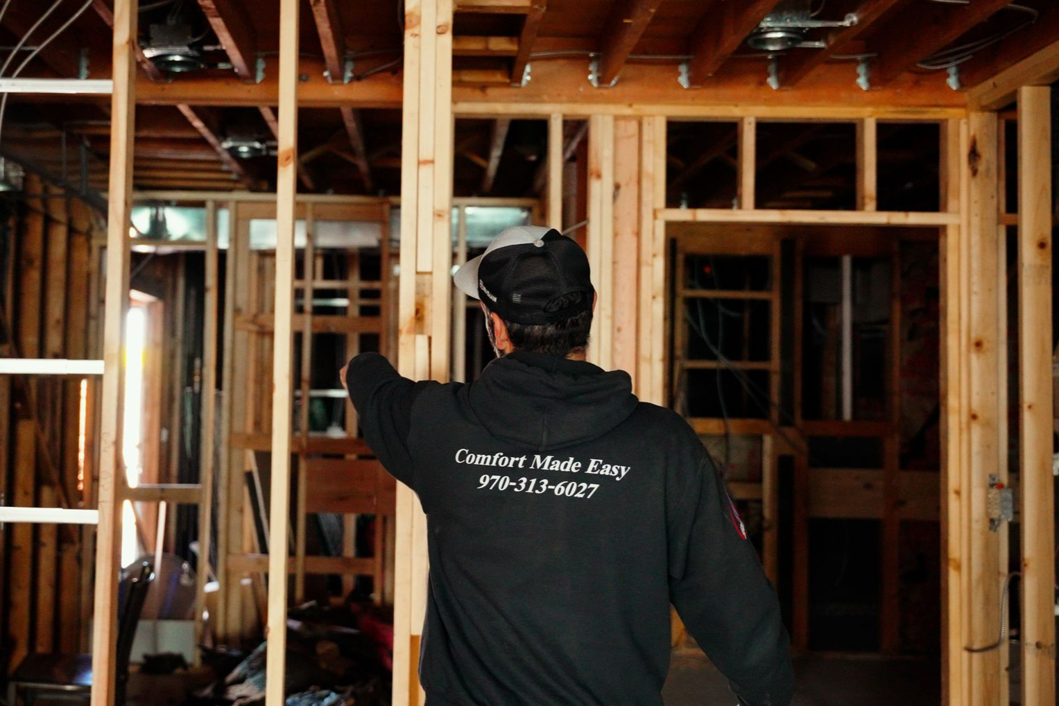 Person in black hoodie inspecting wooden framing inside a construction site.