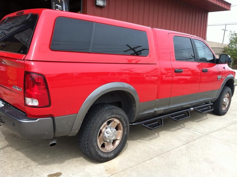 A red truck with a canopy is parked in front of a building.