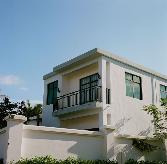 Modern white two-story house with balcony and black railings under a clear blue sky