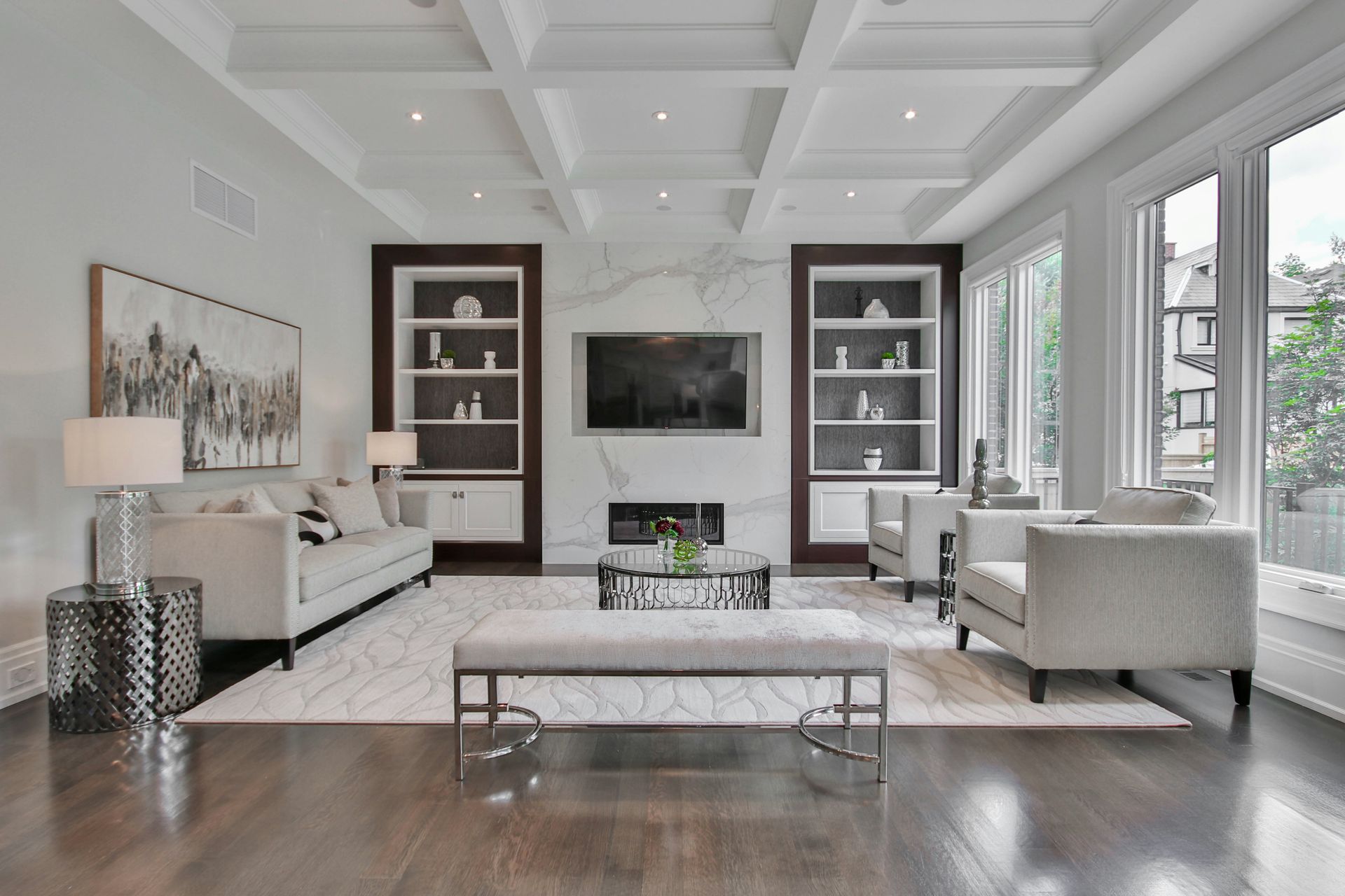 Bright modern living room with white sofas, dark wood floor, wall TV, and large windows