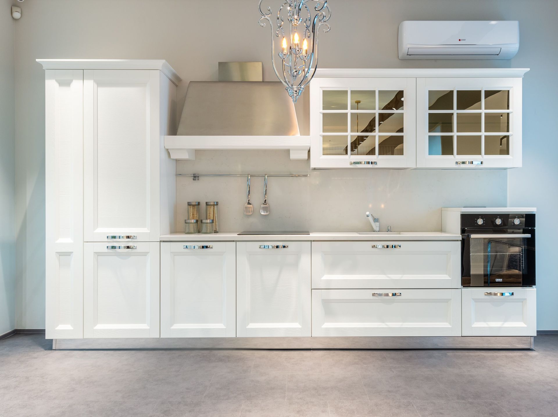 Bright modern white kitchen with cabinets, island, chandelier, and wall-mounted air conditioner