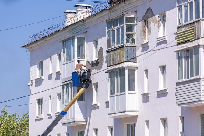 Worker on a ladder repairing a white apartment building exterior under a blue sky