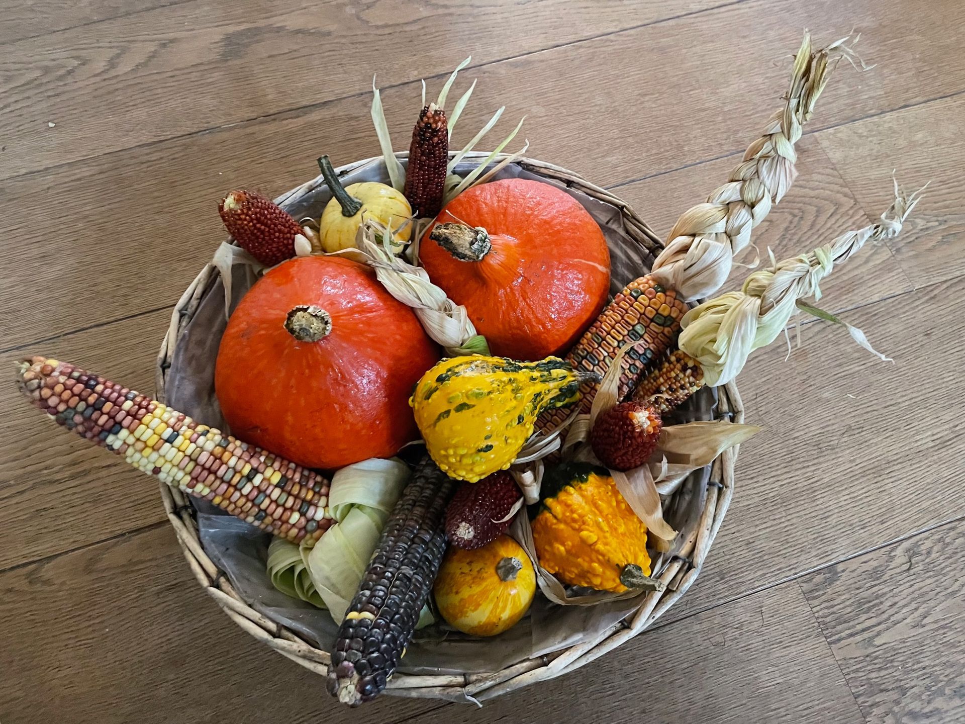 En kurv fyldt med græskar og majskolber på et træbord