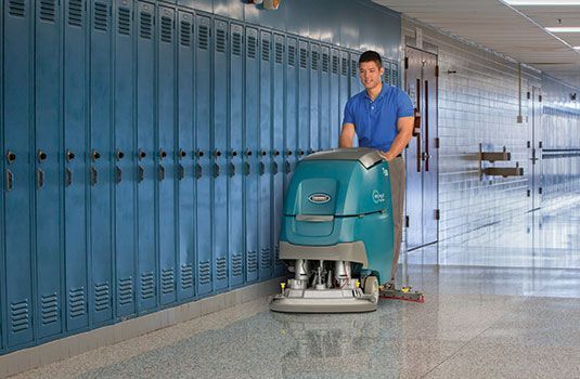 A man is cleaning the floor of a school hallway with a machine.