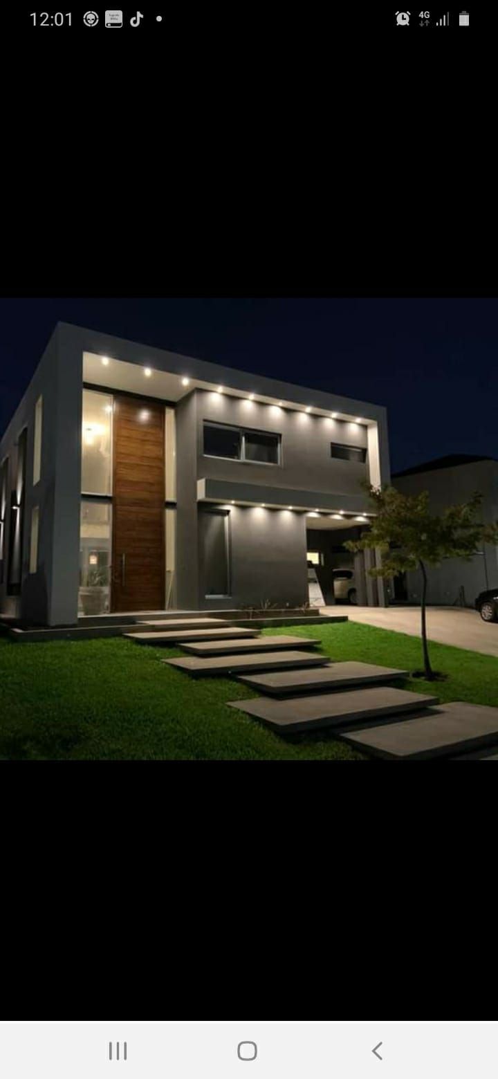 Moderna casa de dos pisos con puerta de madera por la noche, escalones iluminados y un pequeño árbol.