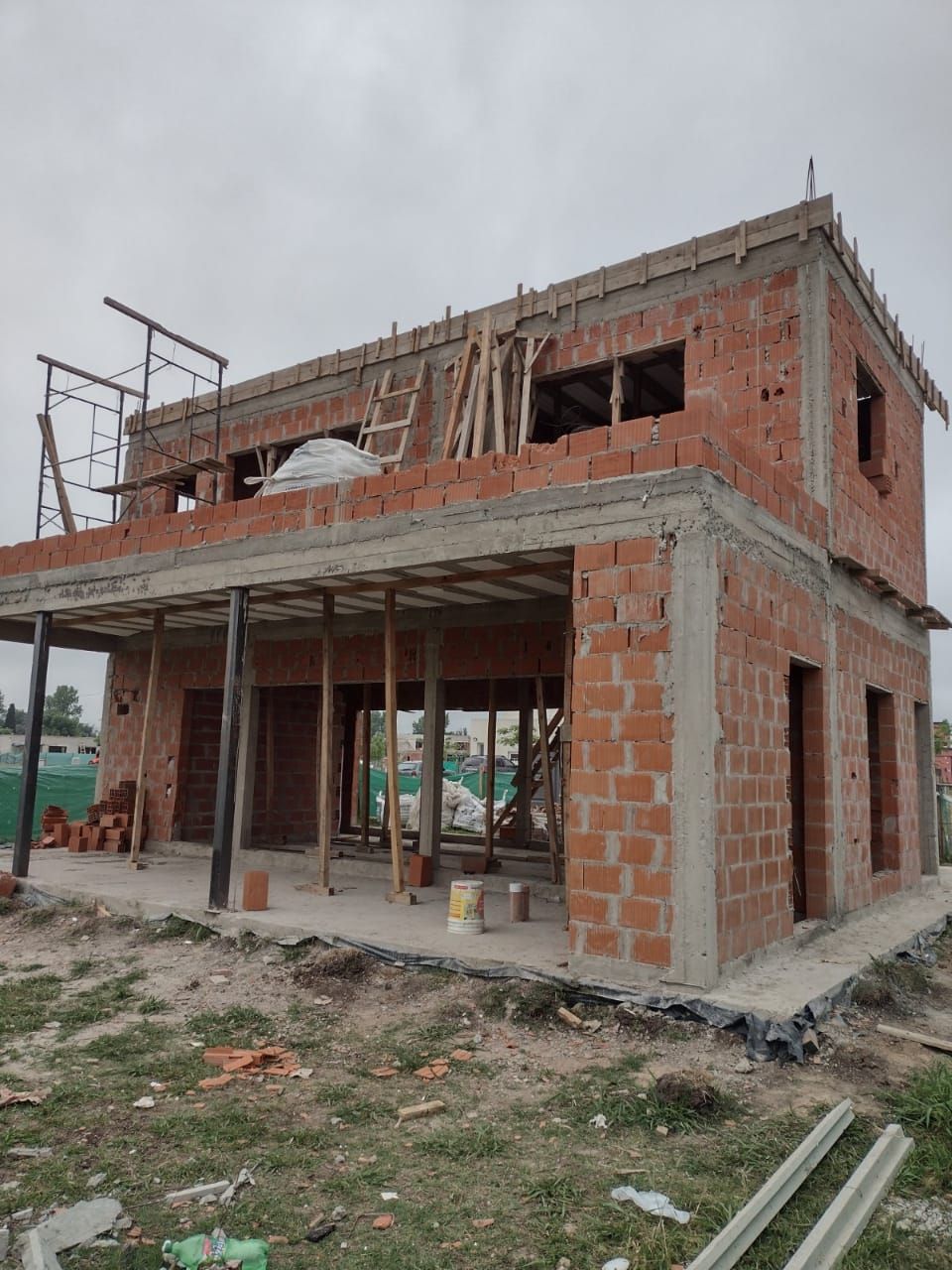 Casa de ladrillo de dos plantas en construcción con porche cubierto y ventanas abiertas.