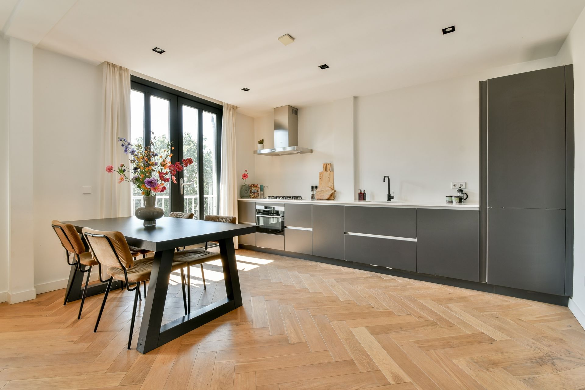 Modern kitchen and dining area with dark gray cabinets, a black table, and wood floors.