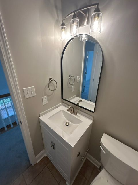 Bathroom with vanity, arched mirror, and toilet. White and gray tones.