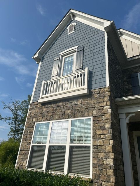 Two-story house with blue siding, stone facade, and a small balcony. Sunny day.