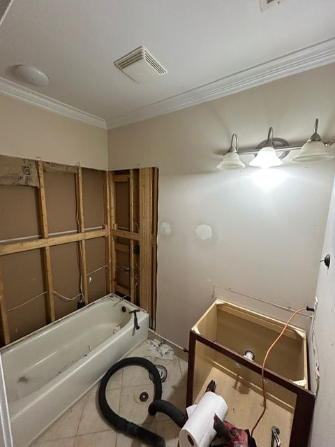 Bathroom renovation in progress, drywall removed. Tub, vanity cabinet, and wiring visible.