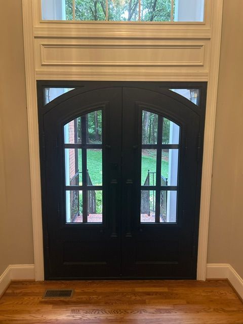 Black double doors with glass panes and a transom window. White trim frames the doors.