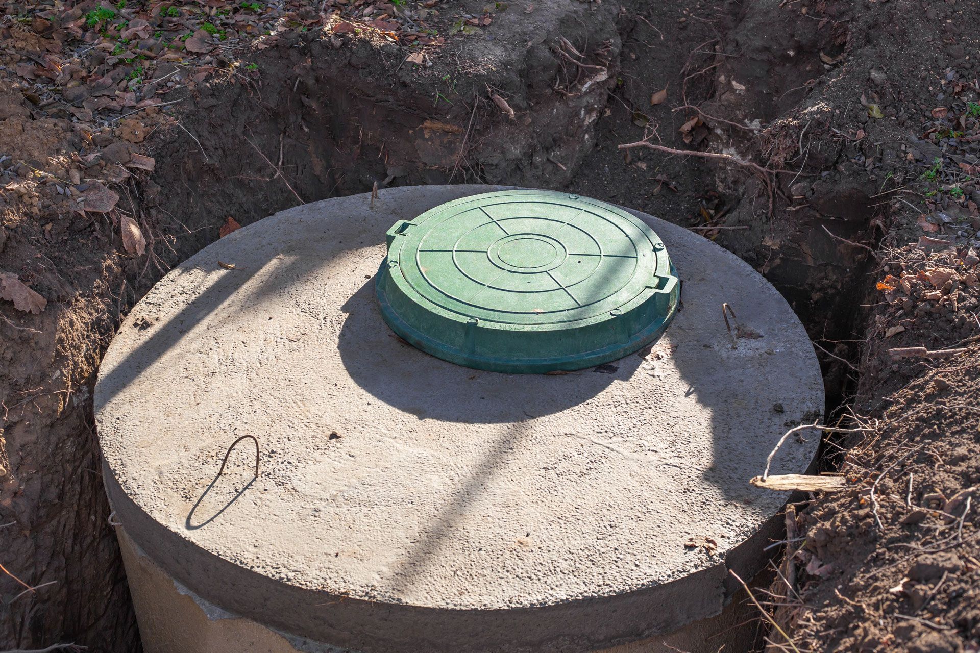 A concrete septic tank with a green lid sits in a dug-out hole in the dirt.