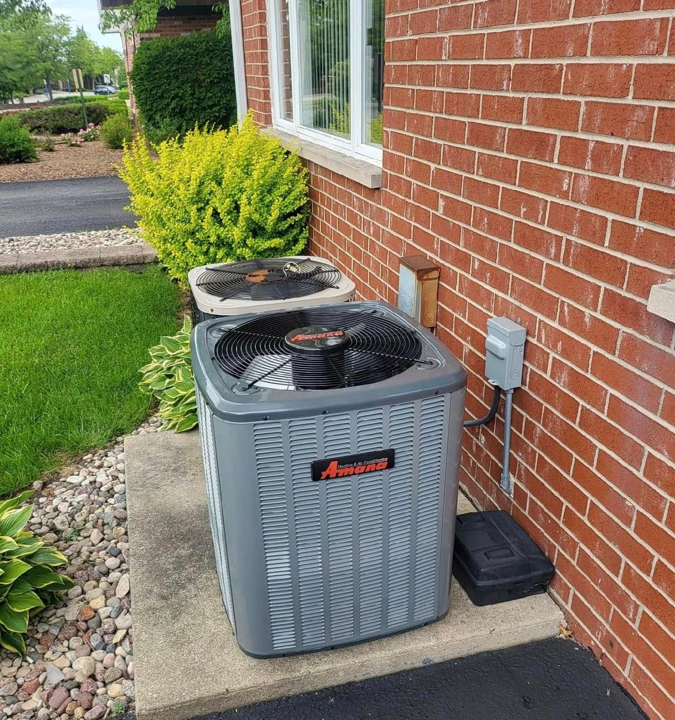 Two Men Are Working On An Air Conditioner - Saint John, IN - Elite Comfort Heating And Air Conditioning LLC