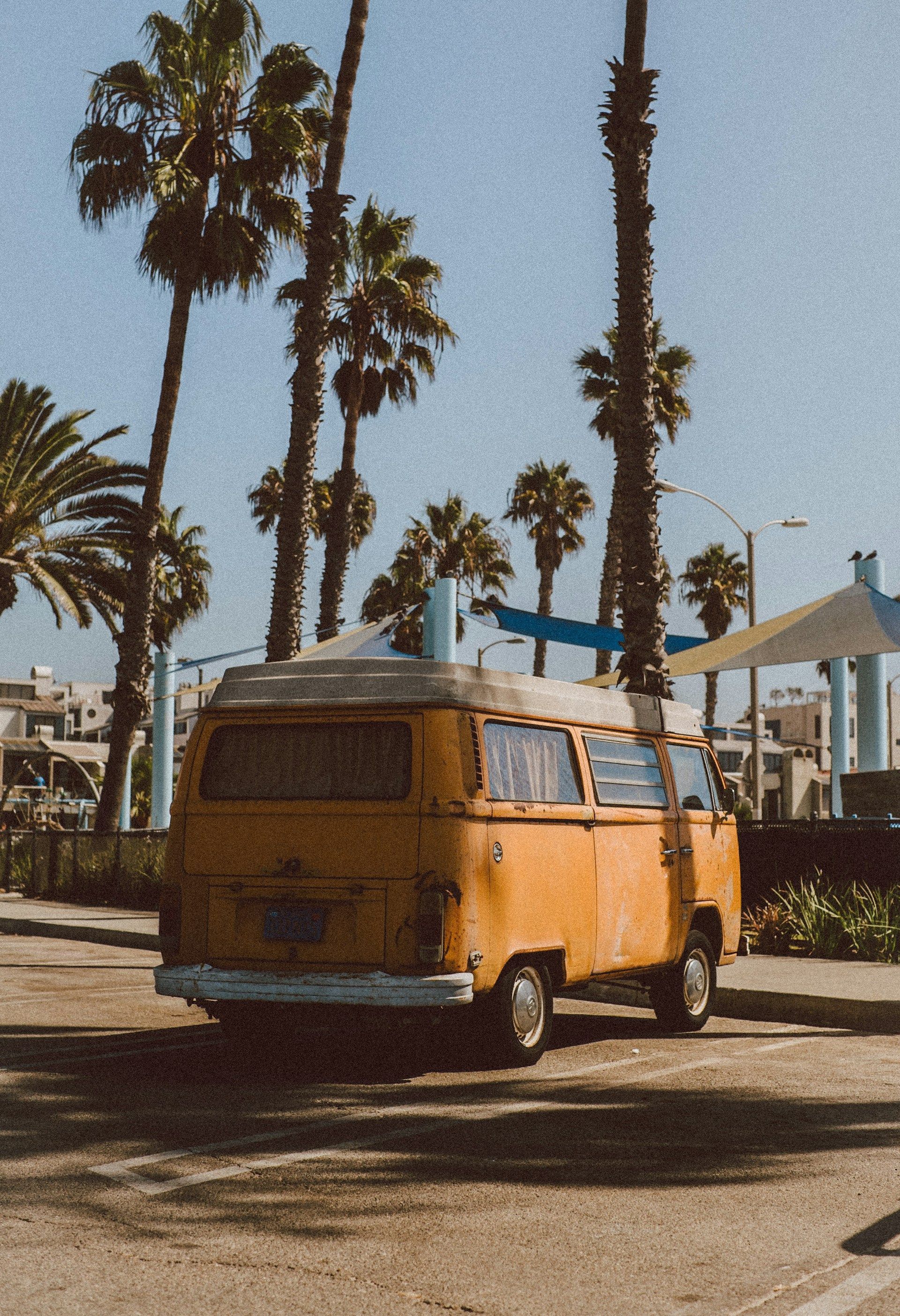 A yellow van is parked in a parking lot with palm trees in the background