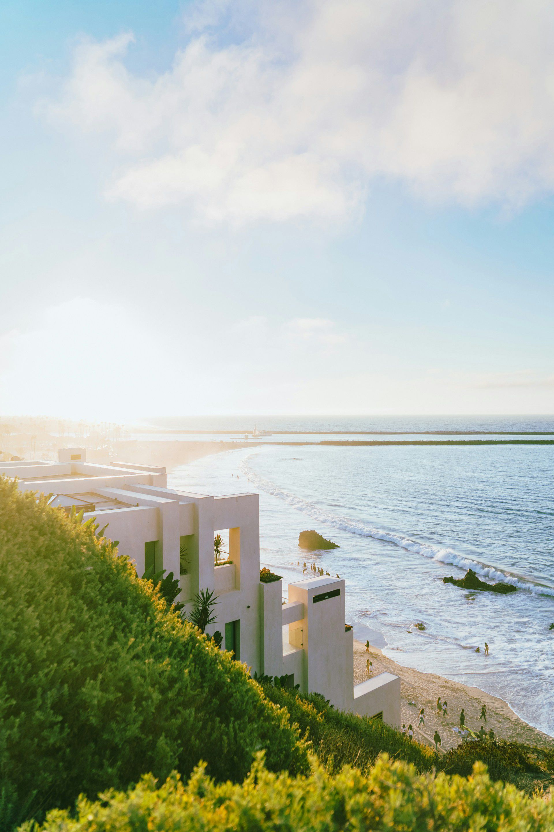 A white building on a hill overlooking the ocean.