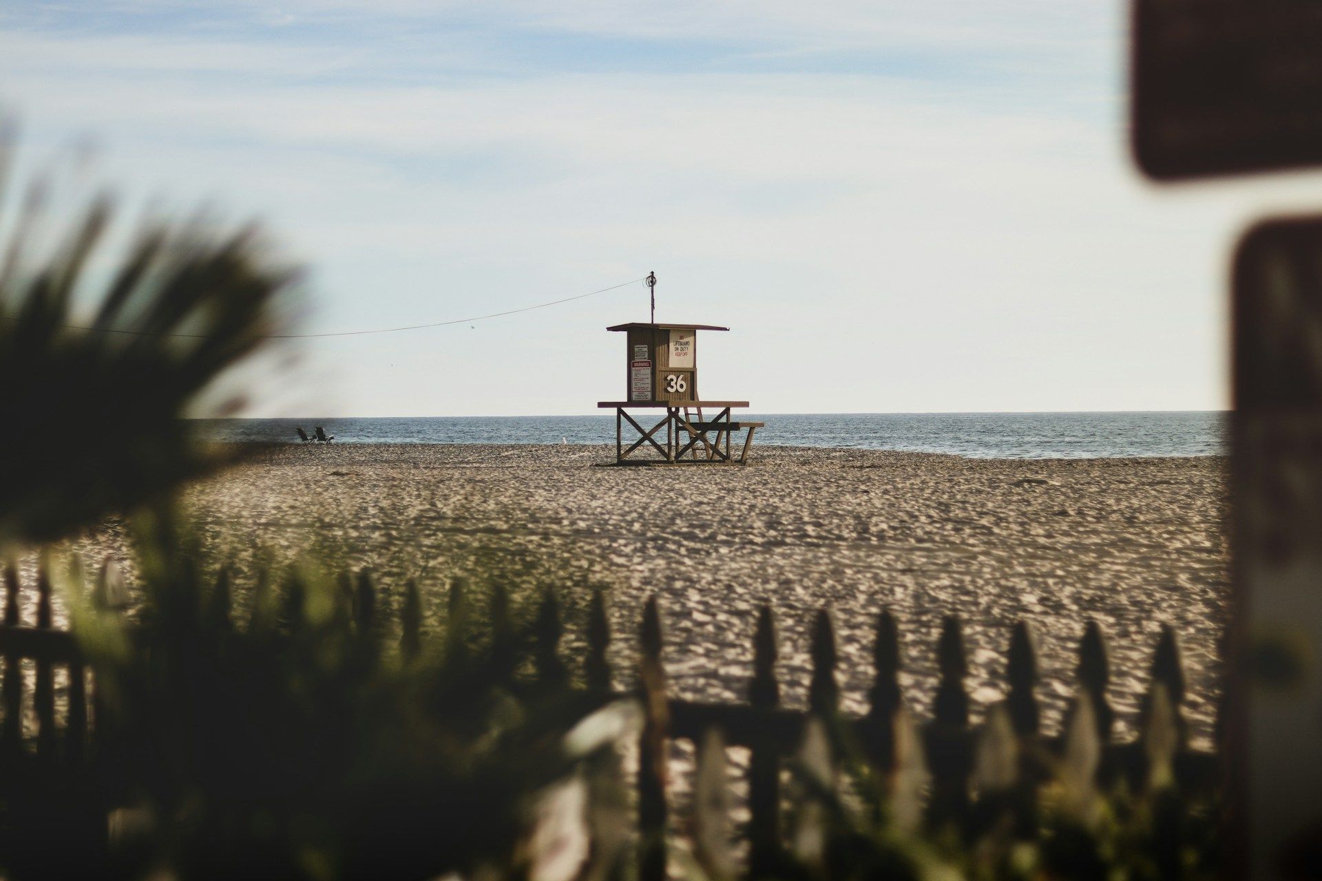 A lifeguard tower on a beach with a fence in the foreground