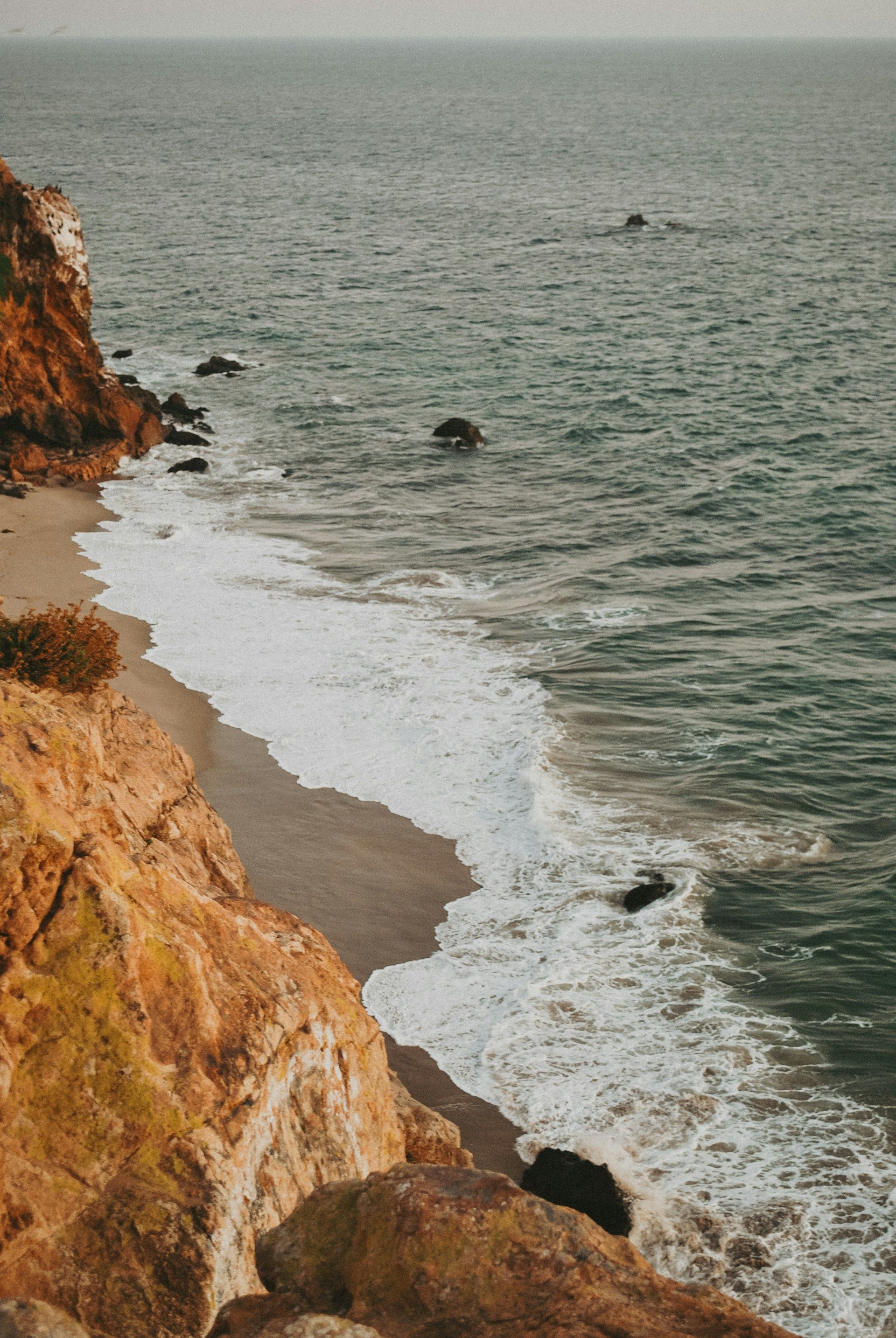A view of a beach from a cliff overlooking the ocean.