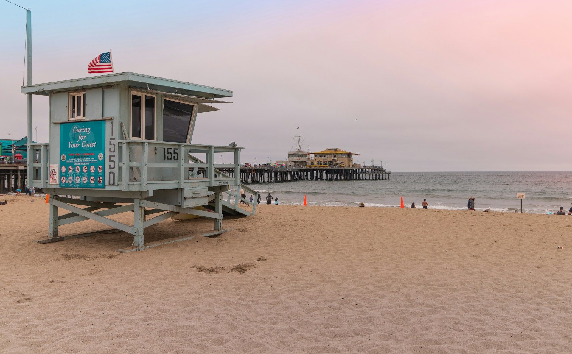 A lifeguard tower on a beach with a pier in the background.