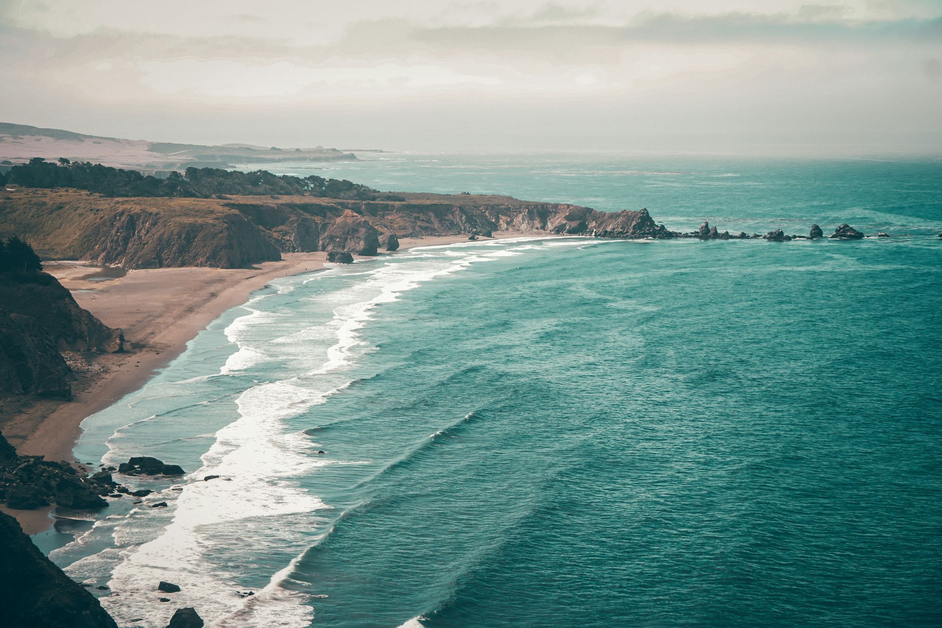 An aerial view of a beach with waves crashing on the shore.