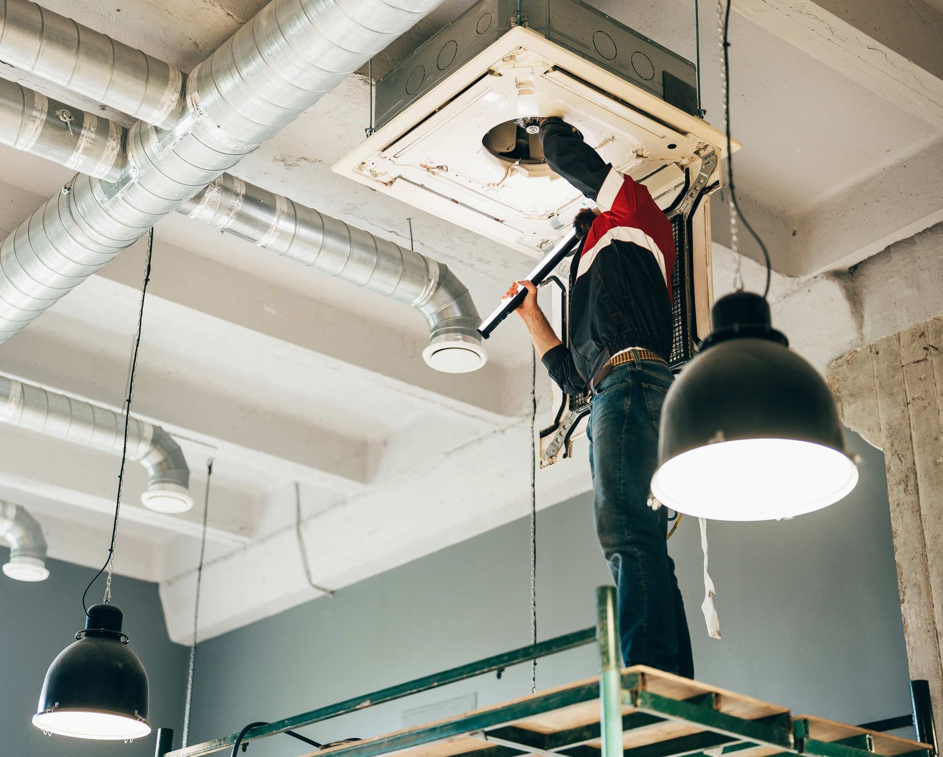 Person on scaffolding inspecting ceiling ventilation system.