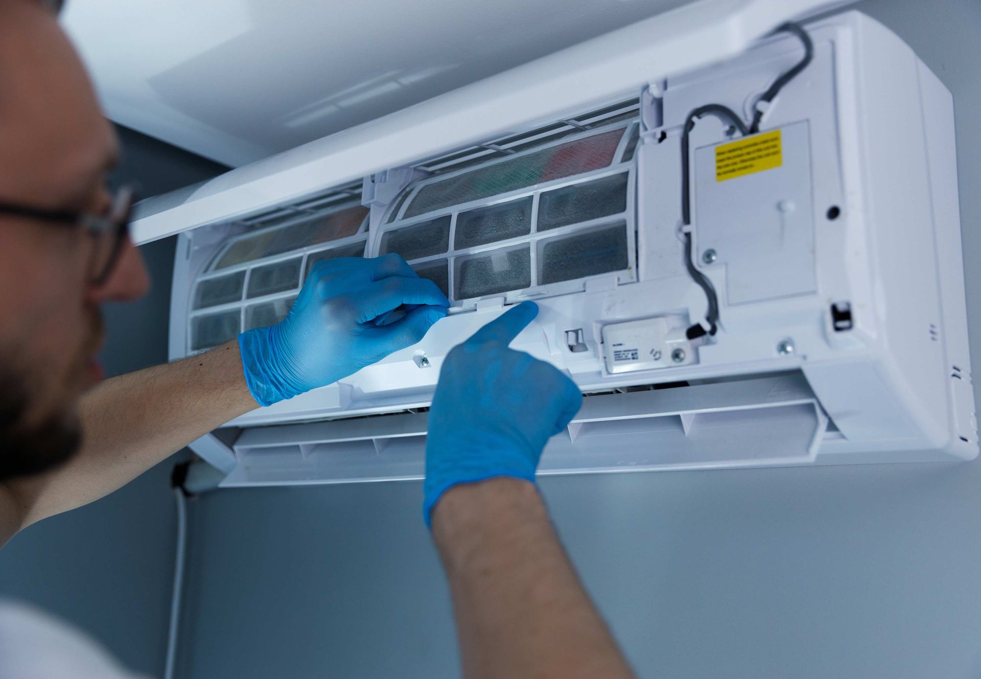 Person wearing blue gloves cleaning an air conditioner filter.