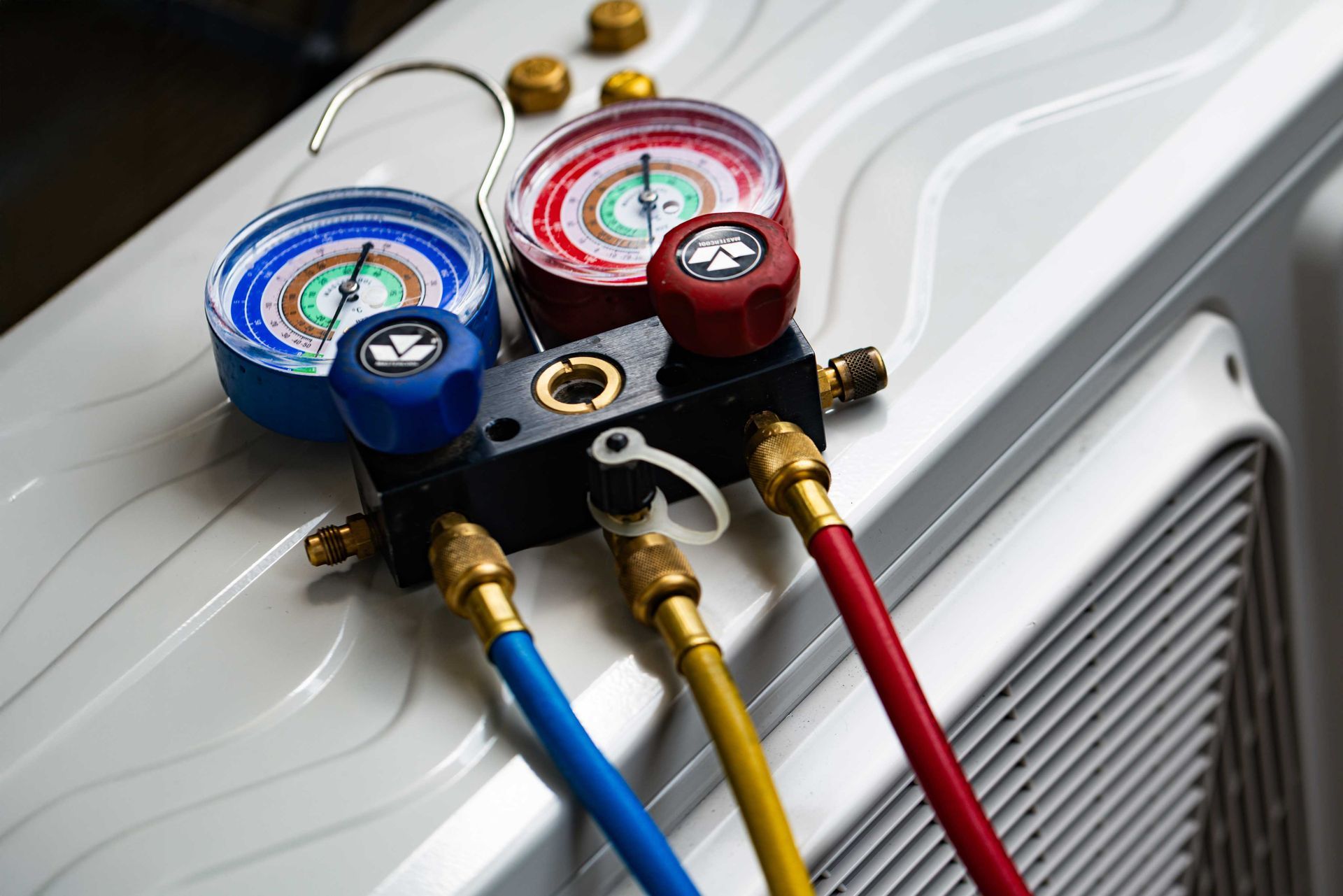 Close-up of air conditioning unit with gauges and colored hoses attached for repair.