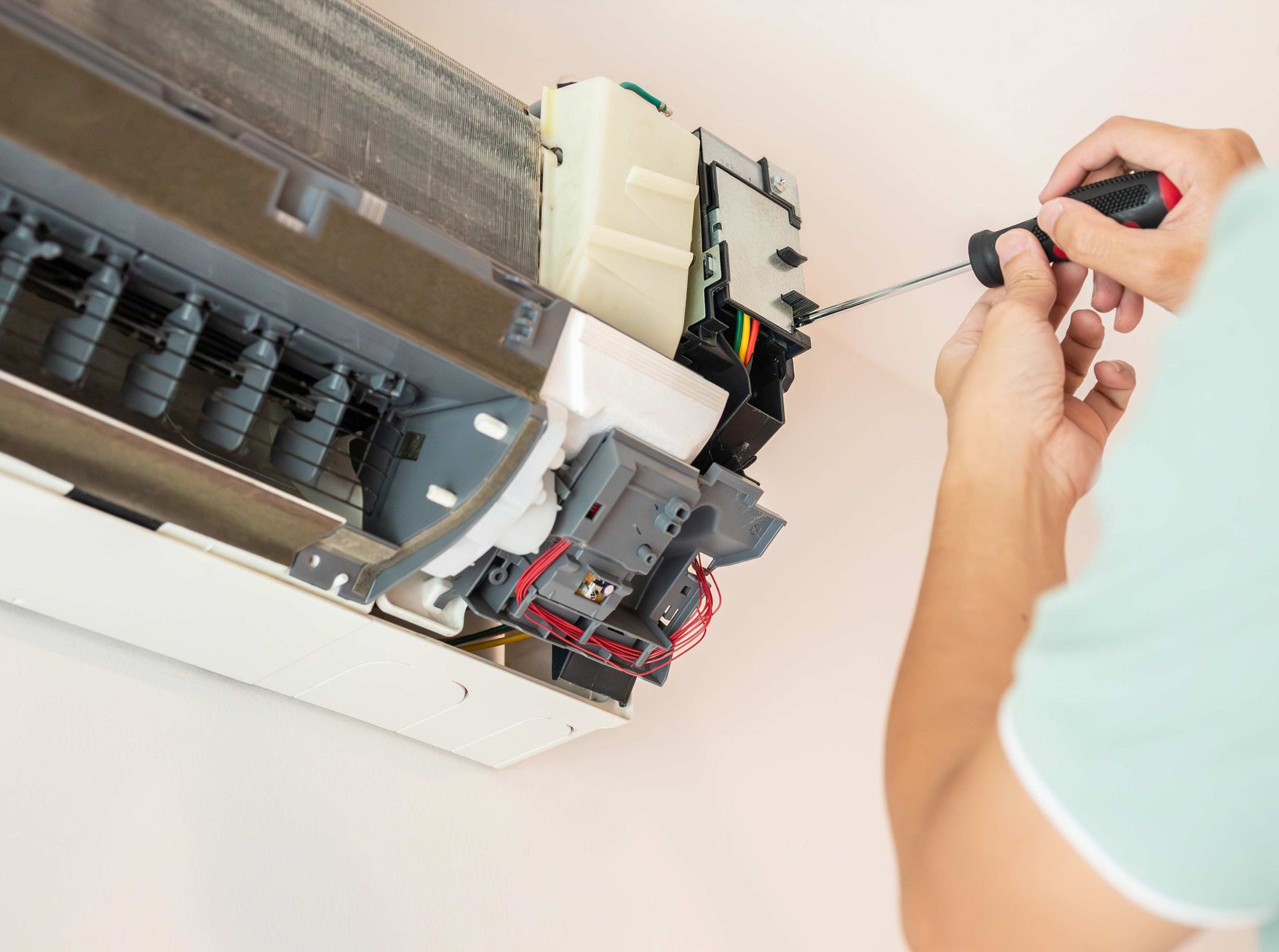Person fixing an air conditioner with a screwdriver. White unit on a wall.
