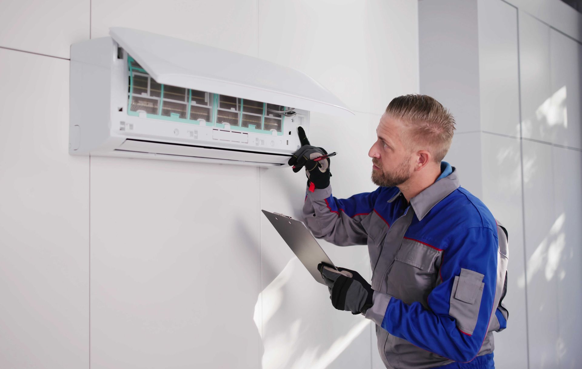 Technician inspecting an air conditioning unit on a white wall, holding a clipboard.