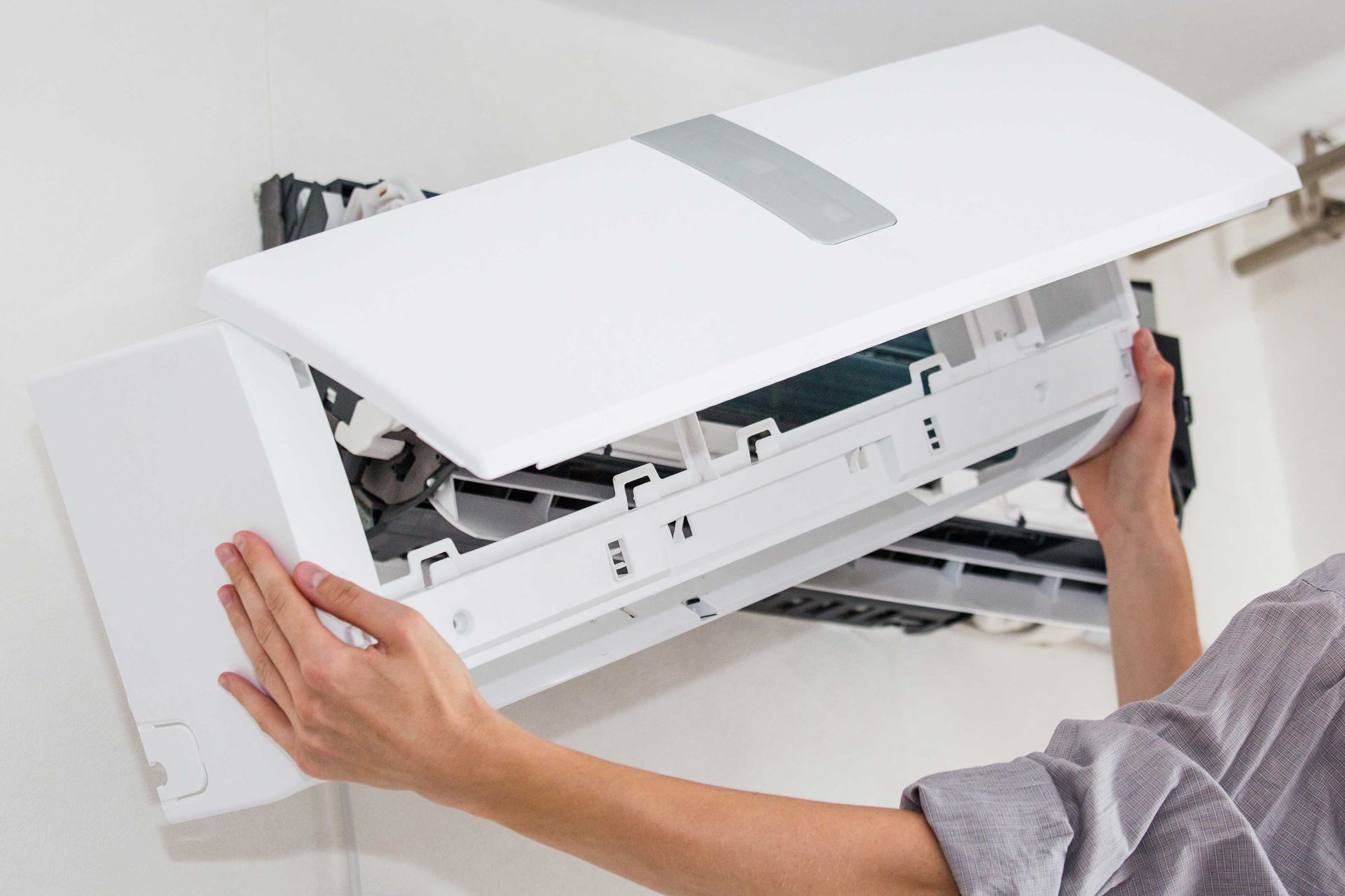 Person removing the cover of a white air conditioning unit mounted on a wall.