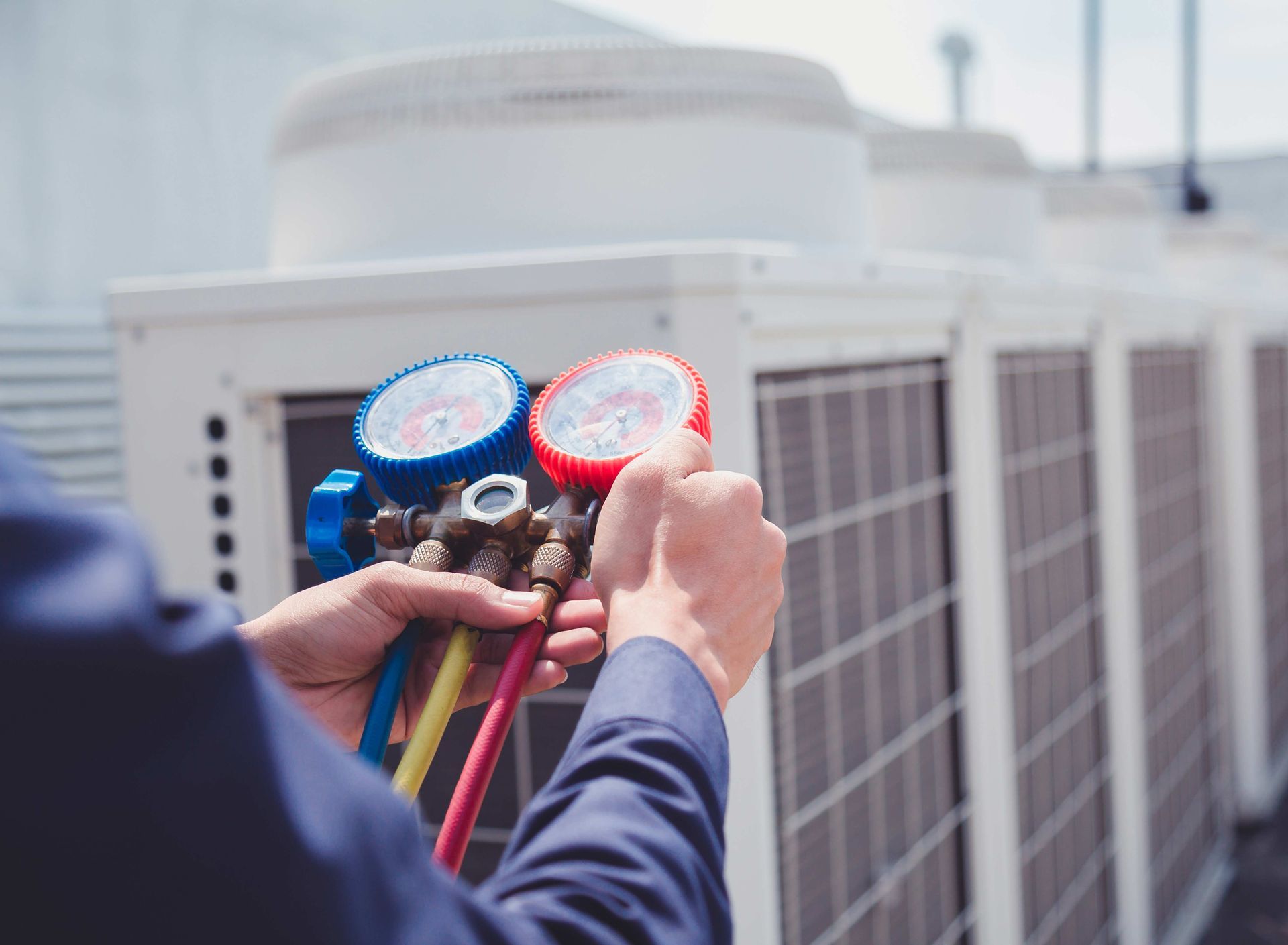 A person holding gauges, checking air conditioning units on a rooftop.