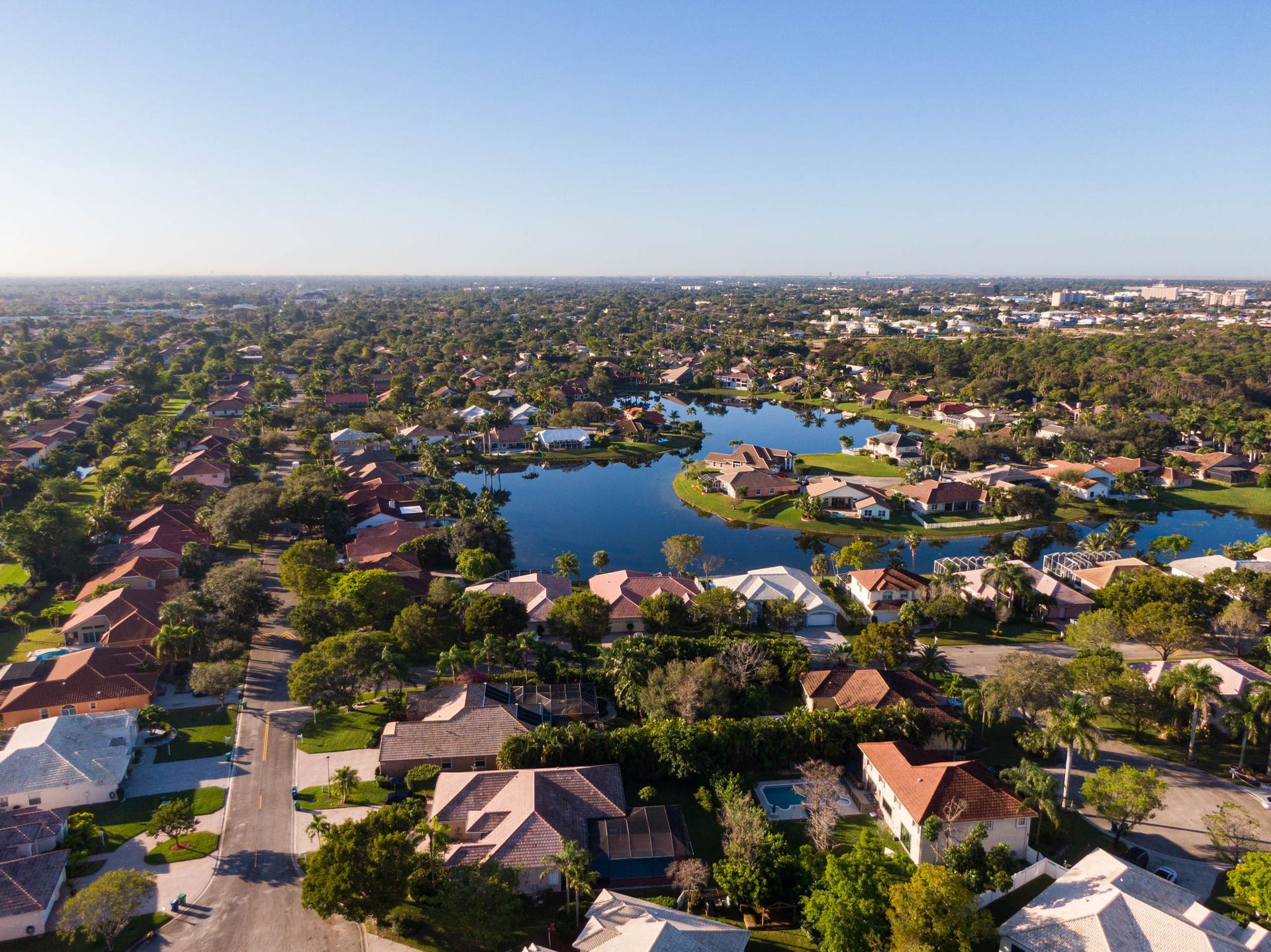 Aerial view of suburban homes in Coral Springs, FL, surrounding a lake; trees and blue sky.