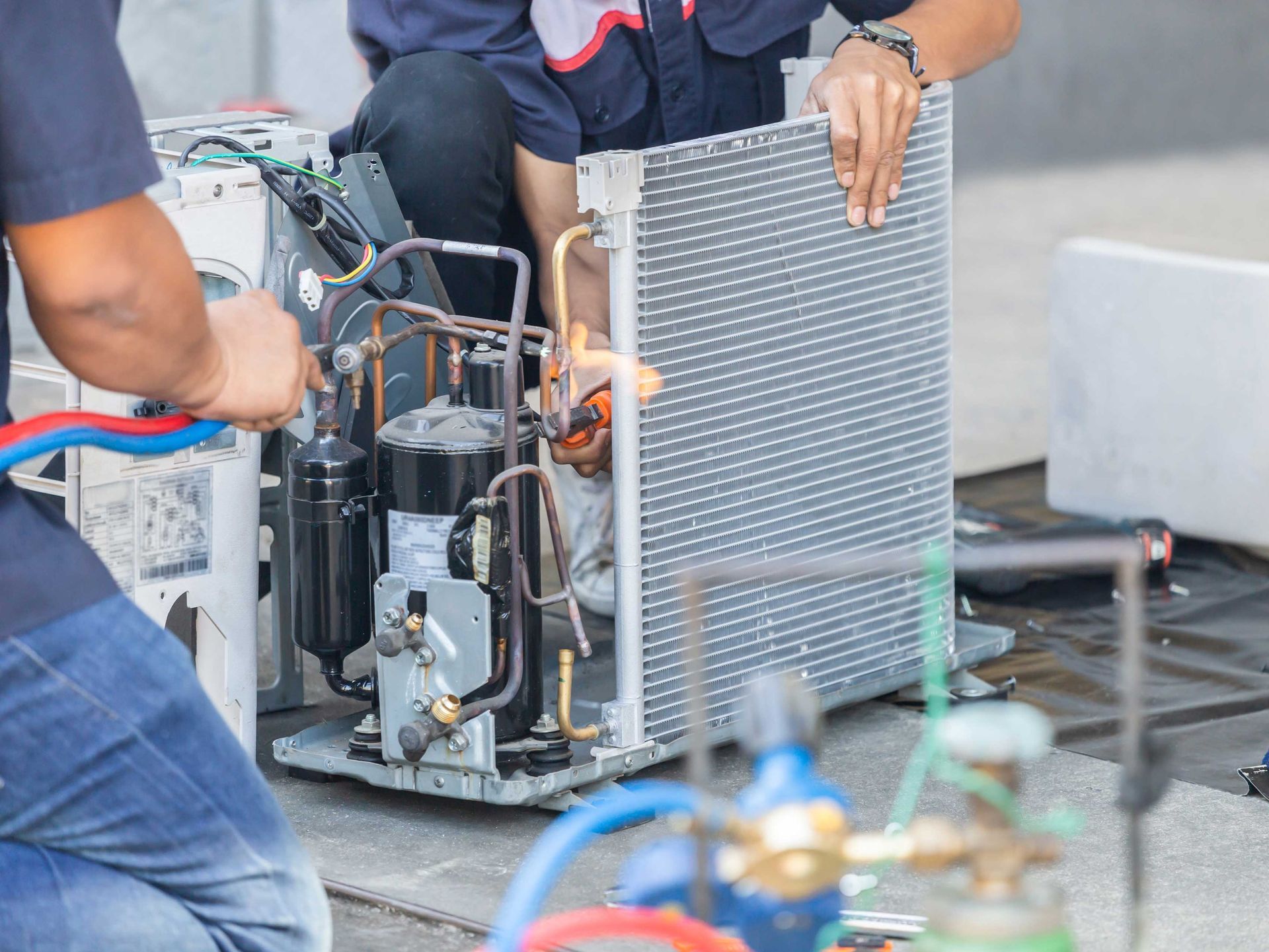 Two technicians repairing air conditioning unit outdoors, using tools and equipment.