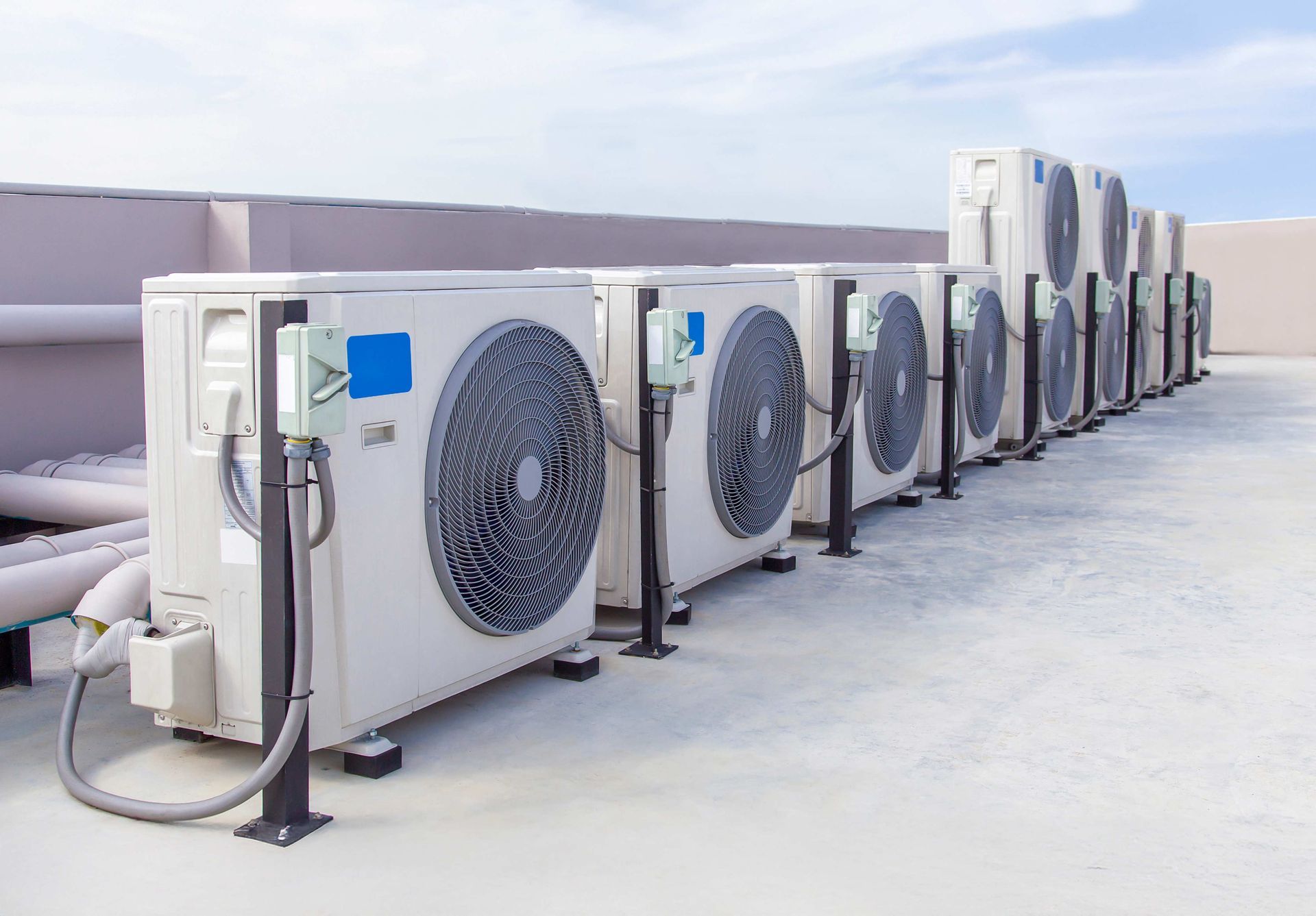 Row of white air conditioning units on a rooftop, against a blue sky.