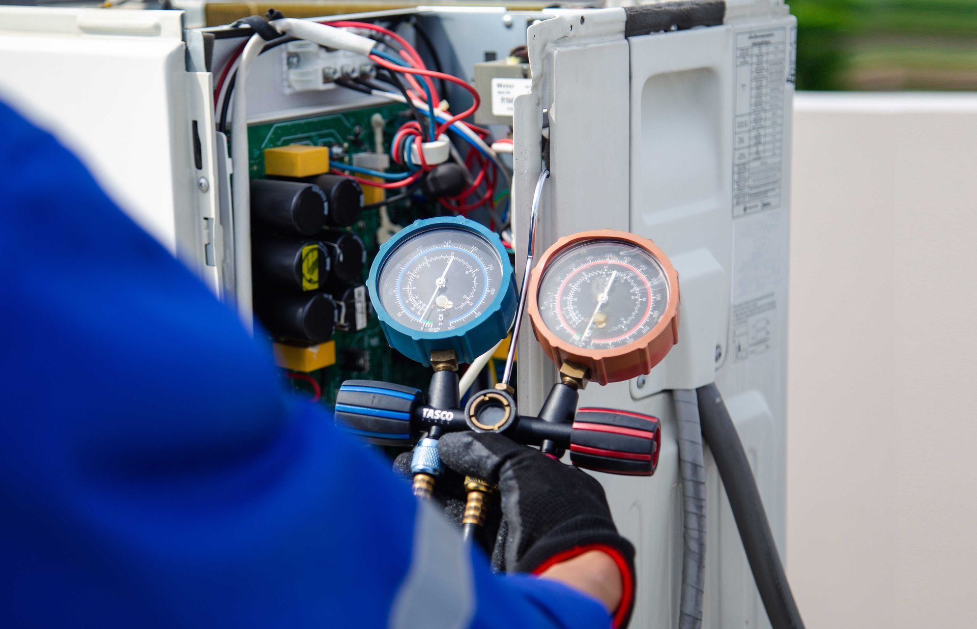 HVAC technician with gauges attached to an air conditioning unit for servicing.