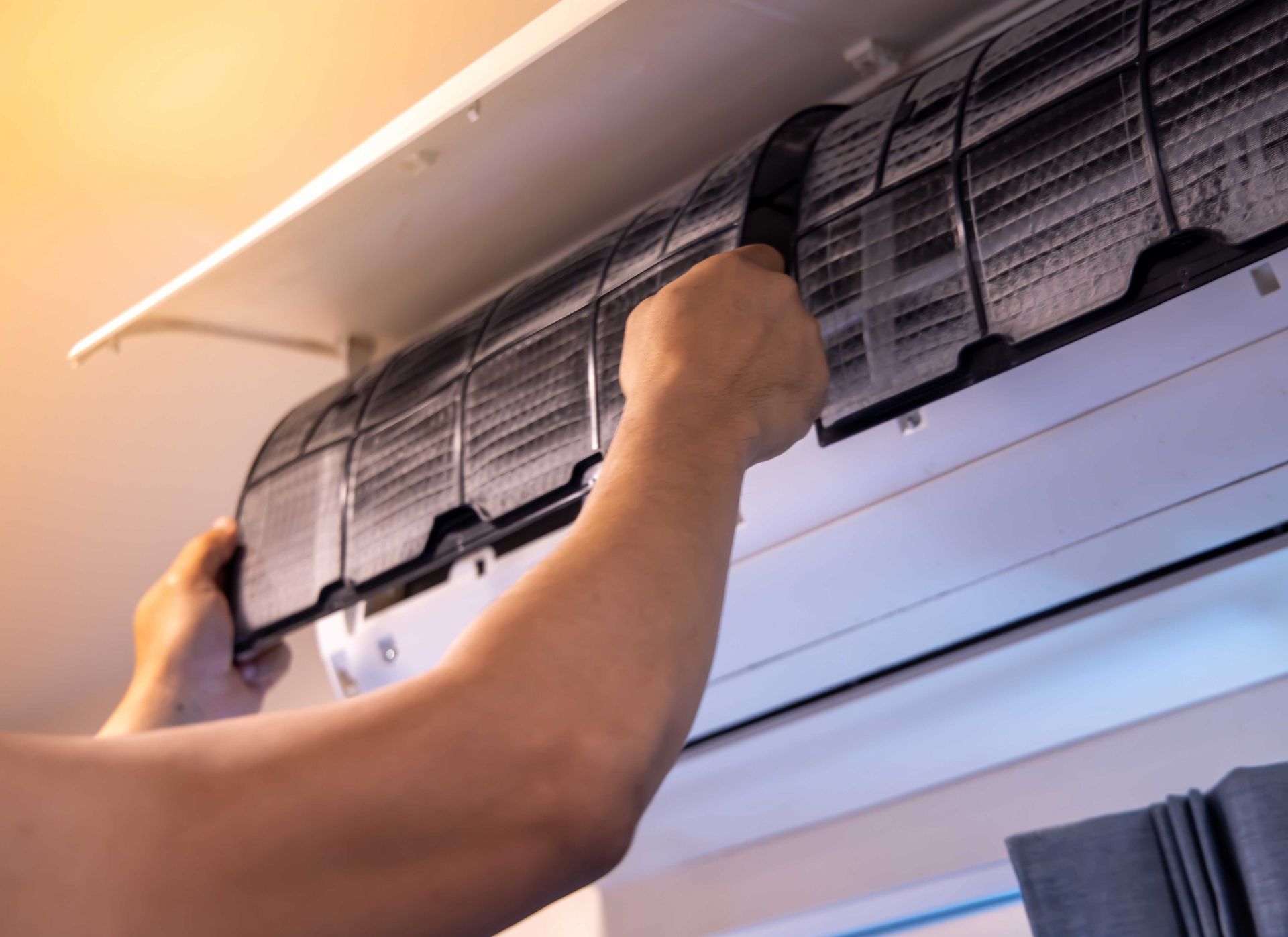 Person removing the air filter from a white air conditioning unit mounted on a ceiling.
