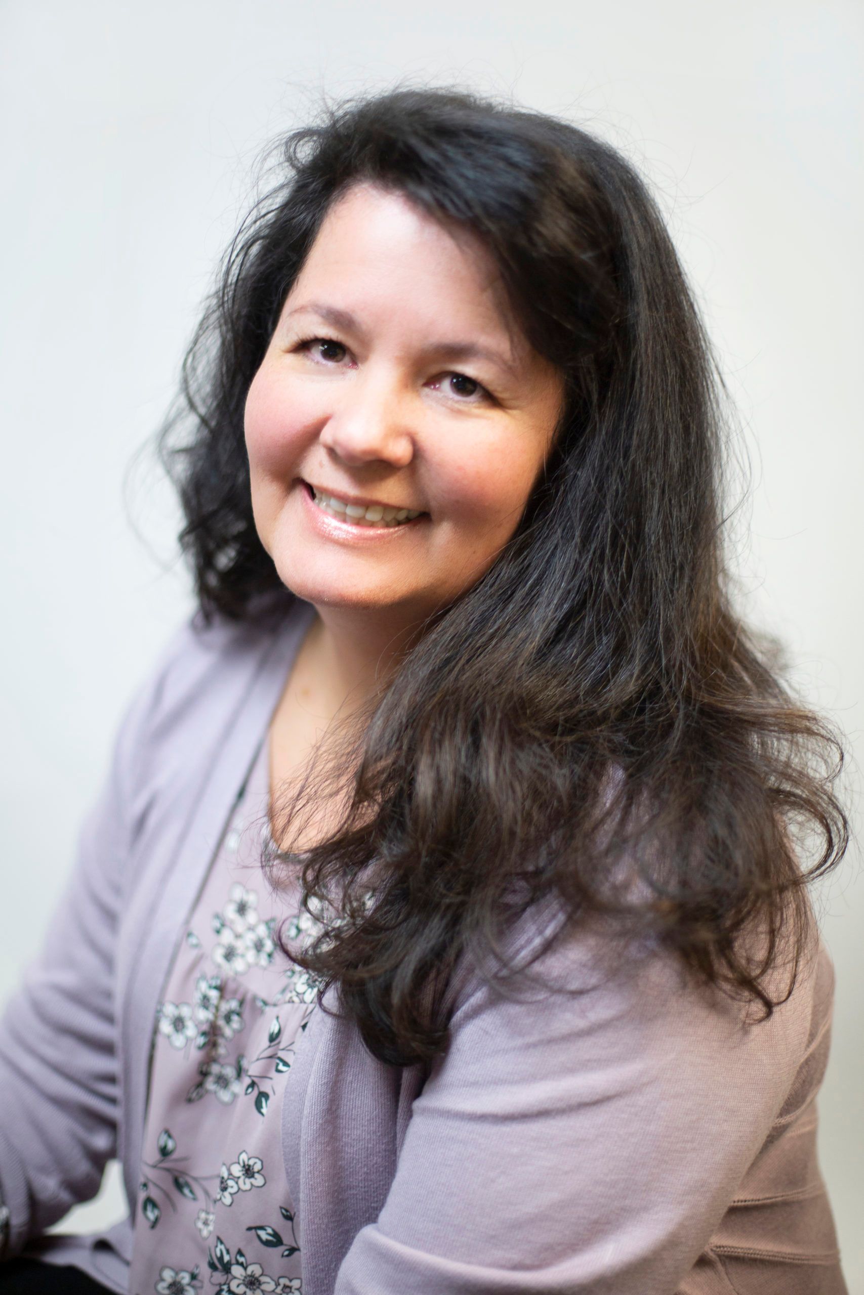 A woman with long hair is wearing a purple sweater and smiling for the camera.