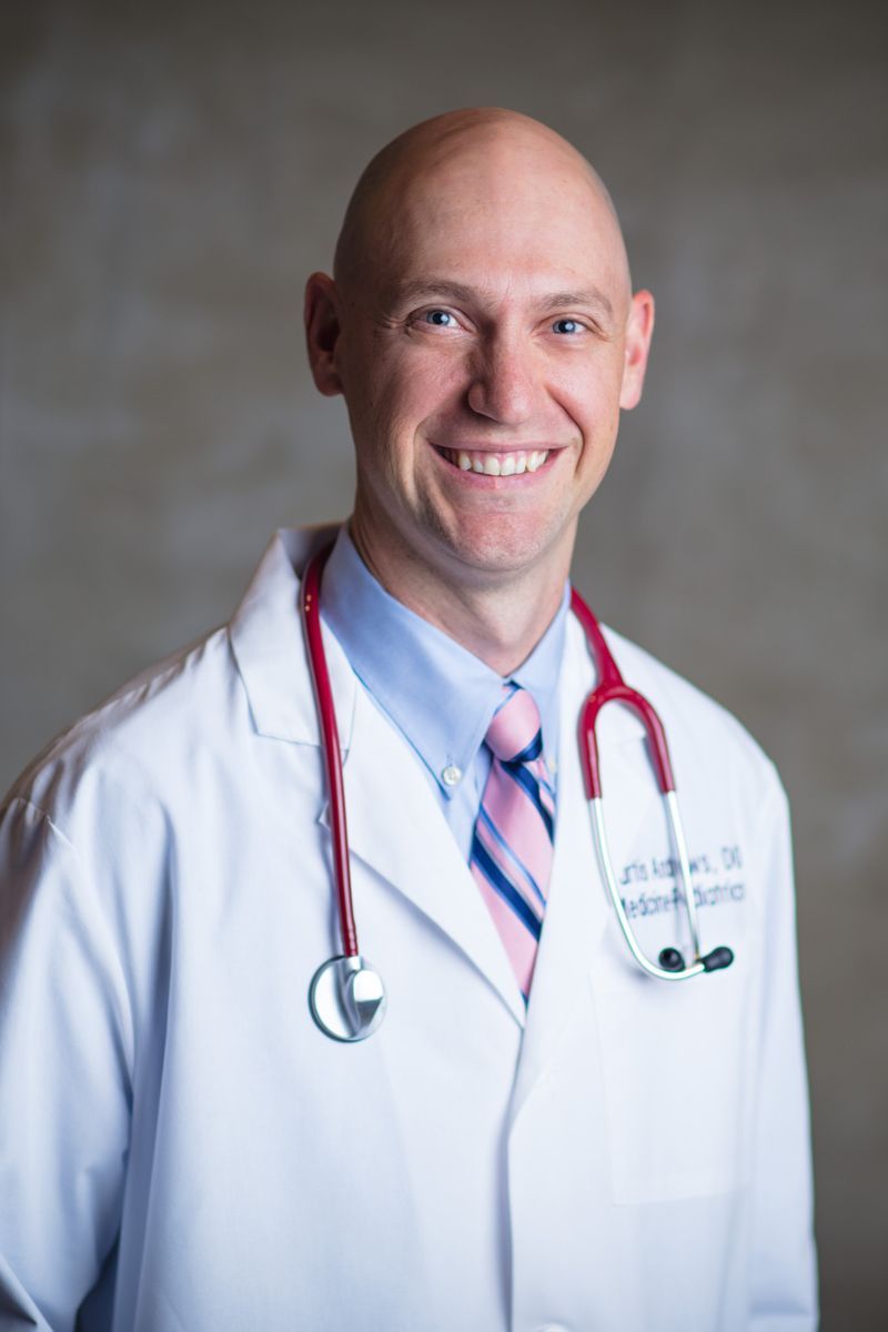 A man in a white coat and tie with a stethoscope around his neck.